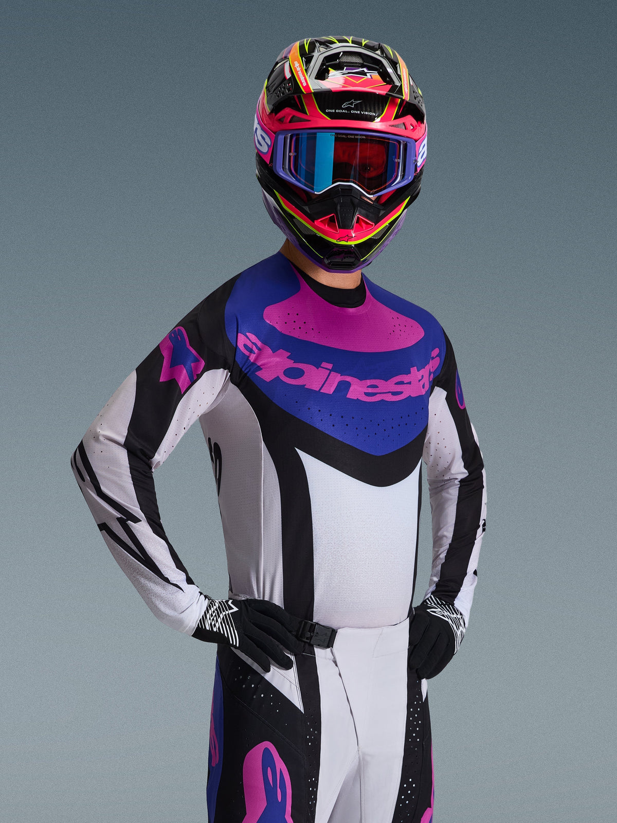 Jersey Techstar Knif 2026 de Alpinestars, jersey de motocross, negro, gris claro y morado, llevado por un piloto con equipamiento completo, con un chasis blanco con detalles negros y un panel azul en el pecho con el logotipo de Alpinestars en morado, ajuste de competición de alto rendimiento para off-road.
