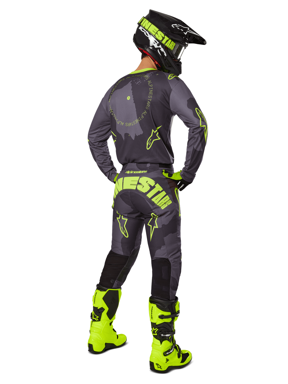 Piloto de motocross visto desde atrás con el jersey y los pantalones Alpinestars 2025 Racer Hollow en Dark Camo Yellow Fluo, con un patrón de camuflaje gris oscuro y detalles en amarillo neón, combinado con un casco a juego negro y amarillo y botas en color amarillo neón brillante.