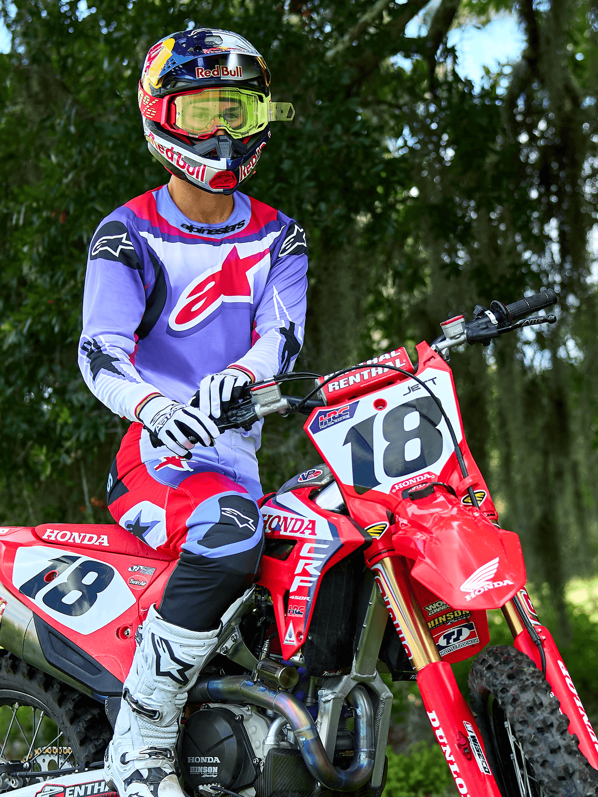 Piloto de motocross en una moto Honda CRF roja, vistiendo el jersey Alpinestars 2025 Fluid Wurx en púrpura y rojo brillante, pantalones a juego en púrpura y rojo, casco Red Bull con gafas amarillas, botas y guantes Alpinestars blancos, equipamiento profesional de MX para conducción todoterreno