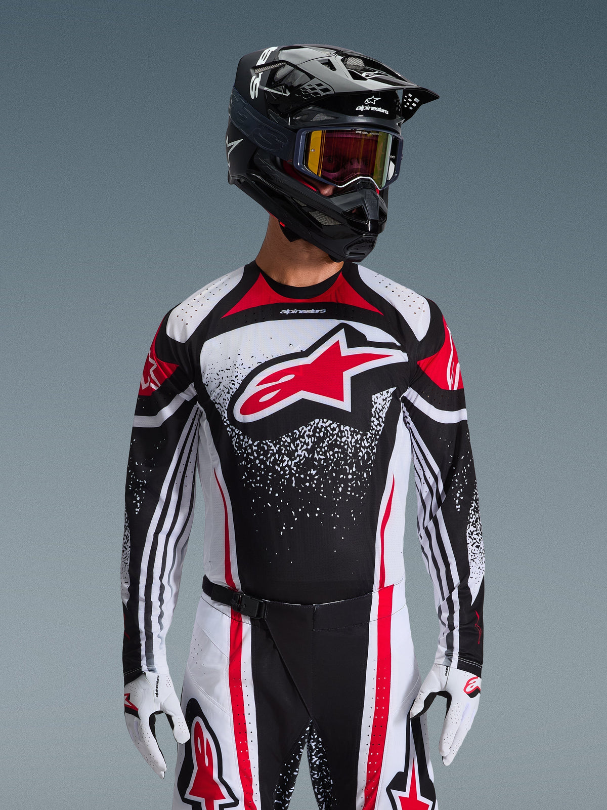 Alpinestars Techstar Nomur Jersey 2026, jersey de motocross, negro, blanco y rojo, usado por un piloto con pantalones a juego, casco negro y guantes blancos, con un gran logotipo rojo de Astars y diseño gráfico moteado, ajuste atlético de competición para todoterreno