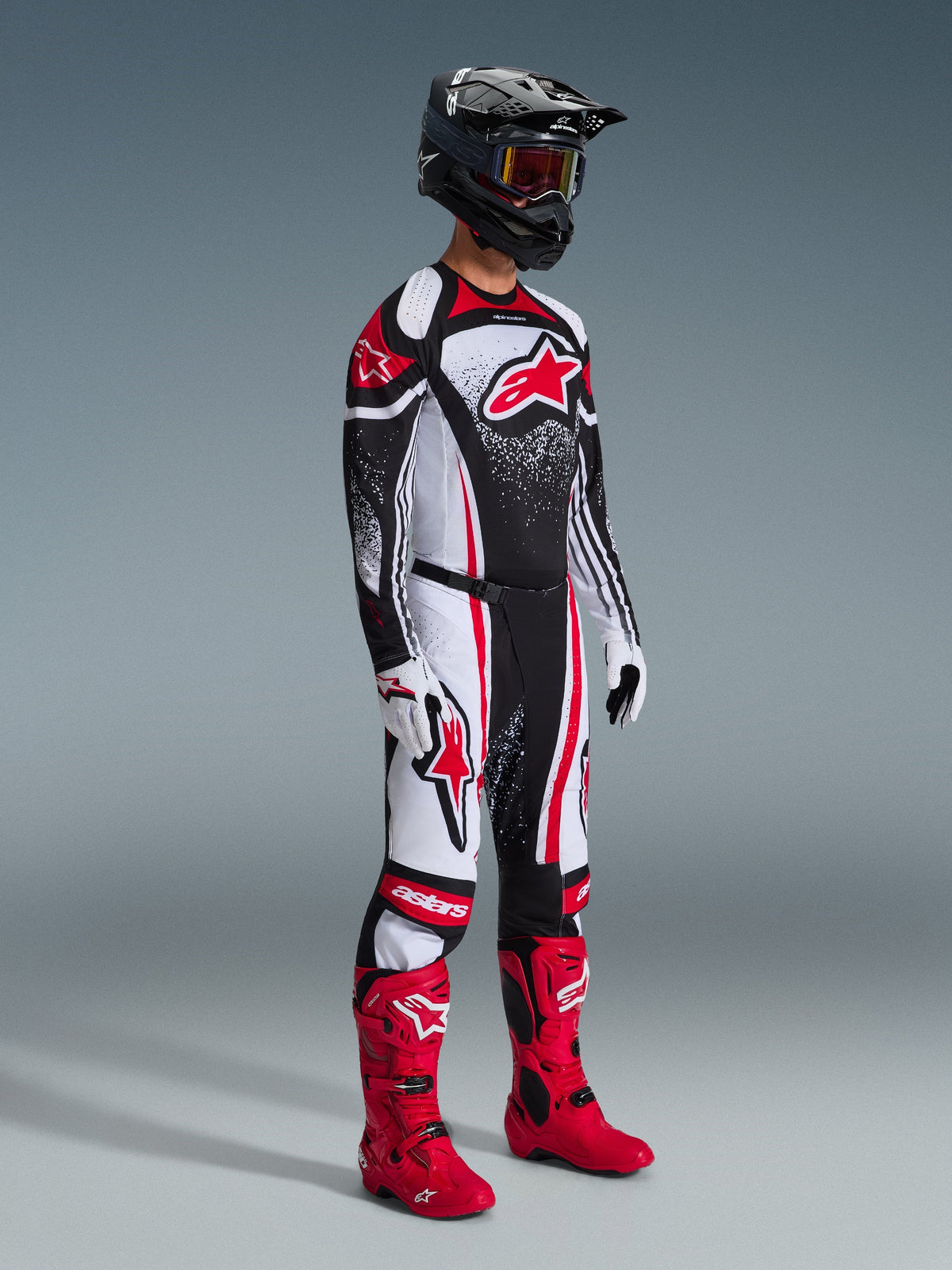 Piloto de motocross con Jersey Techstar Nomur 2026, equipamiento de carreras en negro, blanco y rojo, pantalones a juego con detalles rojos, casco negro, botas de color rojo brillante, guantes blancos y negros, conjunto completo de motocross profesional para competición todoterreno.