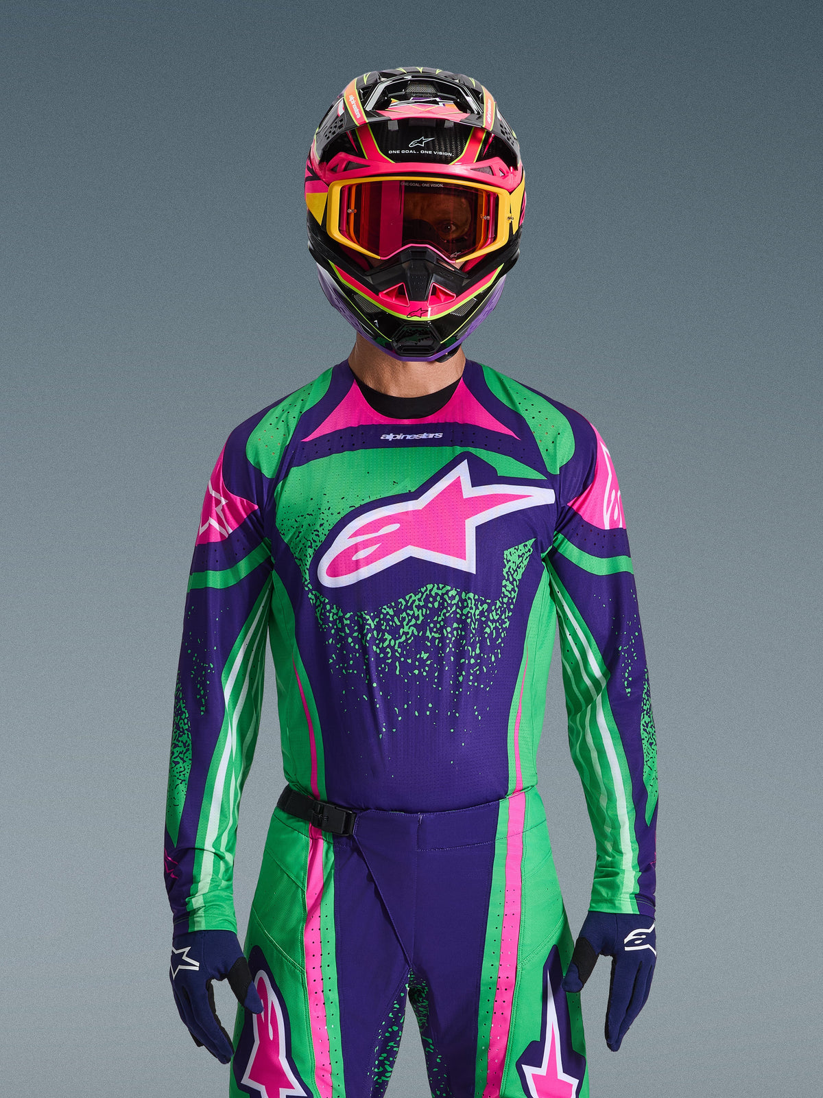 Alpinestars 2026 Techstar Nomur Gear Set, piloto de motocross con jersey de carreras en verde vibrante y púrpura con detalles en rosa, conjunto de equipamiento a juego con casco y gafas multicolores, atuendo de motociclismo off-road de alto rendimiento