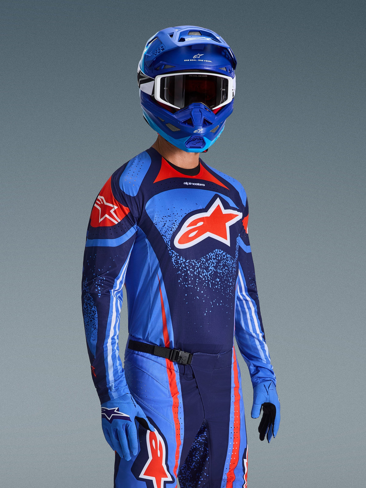 Motocross rider wearing Alpinestars 2026 Techstar Nomur Jersey, Dark Navy Orange and UCLA Blue racing gear, featuring large orange Astars logo, matching blue helmet and gloves, athletic off-road competition outfit.