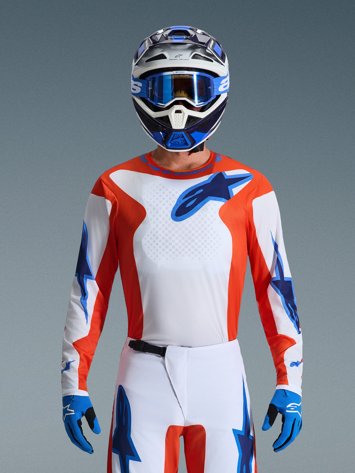 Alpinestars 2026 Fluid Grid Gear Set, piloto de motocross con jersey naranja y blanco con logos de estrellas azules, pantalones blancos con acentos azules, casco azul y blanco a juego con gafas y guantes azules, equipamiento completo para carreras todoterreno