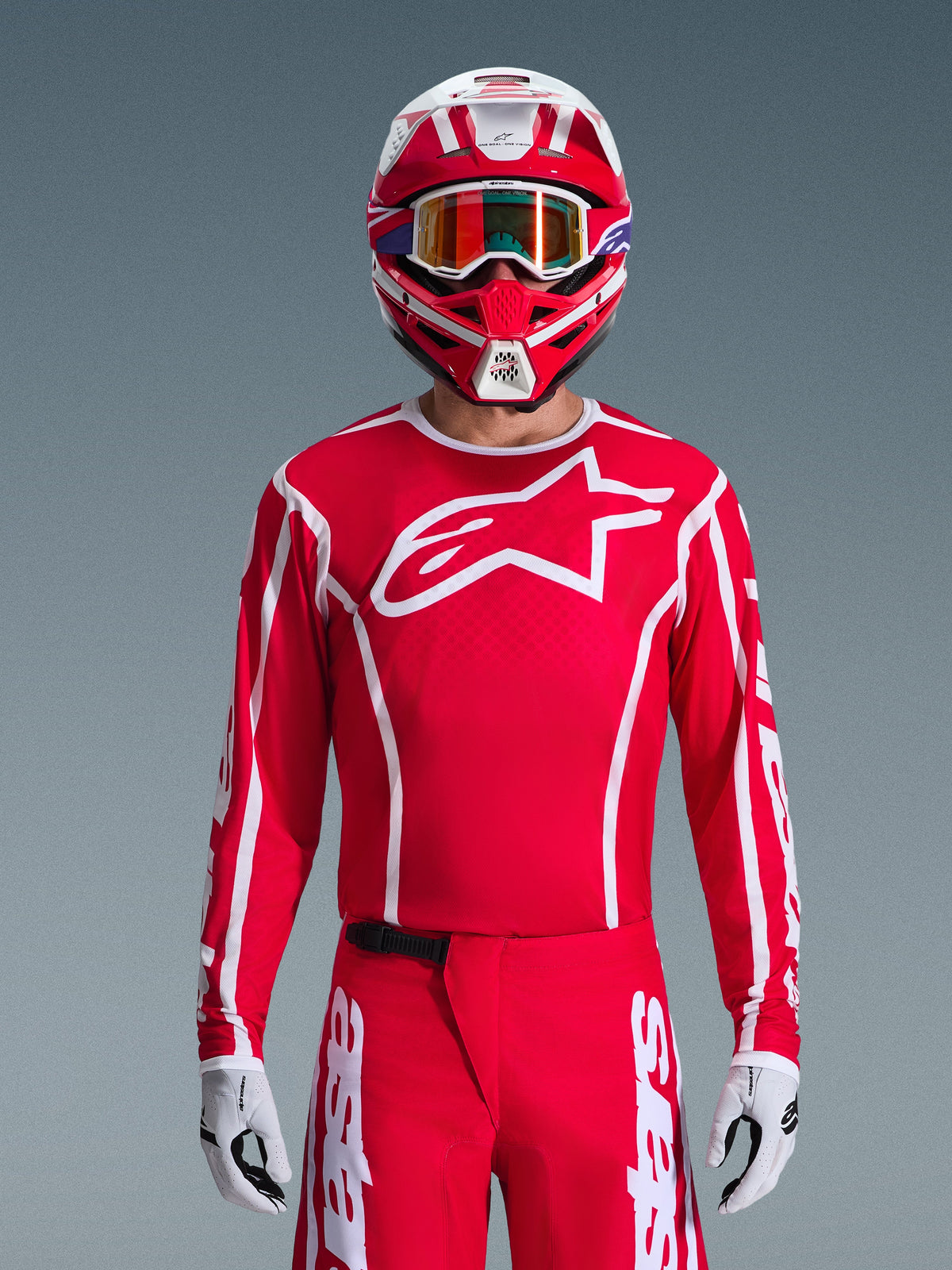 Piloto de motocross con el conjunto completo Alpinestars 2026 Fluid Apex, camiseta roja con un gran logotipo de estrella blanco en el pecho, pantalones rojos a juego con marca en blanco, casco rojo y blanco con gafas iridiscentes, guantes blancos y negros, equipamiento coordinado en rojo y blanco para carreras off-road