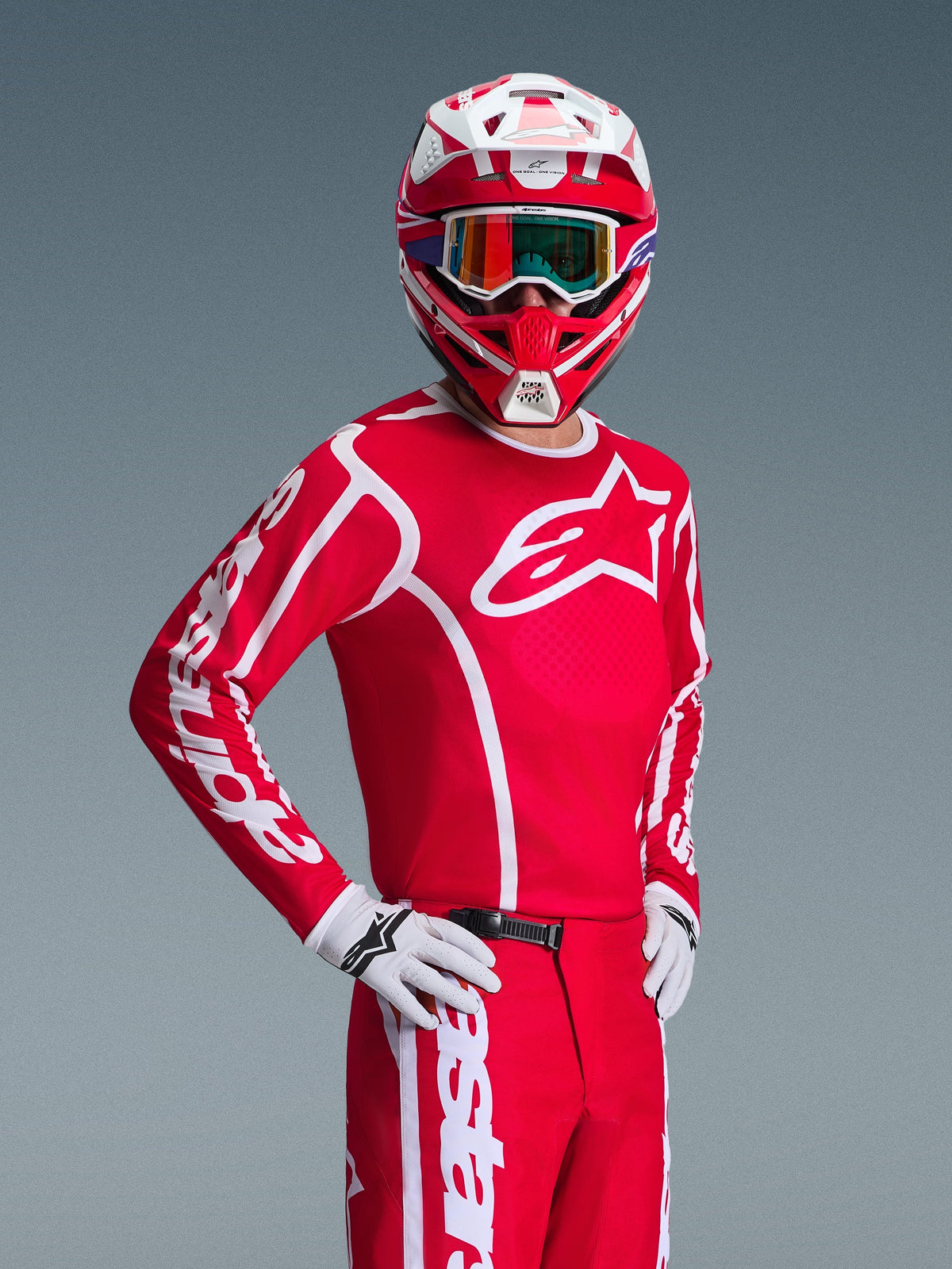 Piloto de motocross con el jersey Alpinestars Fluid Apex 2026 en rojo y blanco, casco a juego en rojo y blanco con gafas, guantes blancos y pantalones rojos, con logotipos blancos llamativos y ajuste atlético, conjunto coordinado para carreras todoterreno