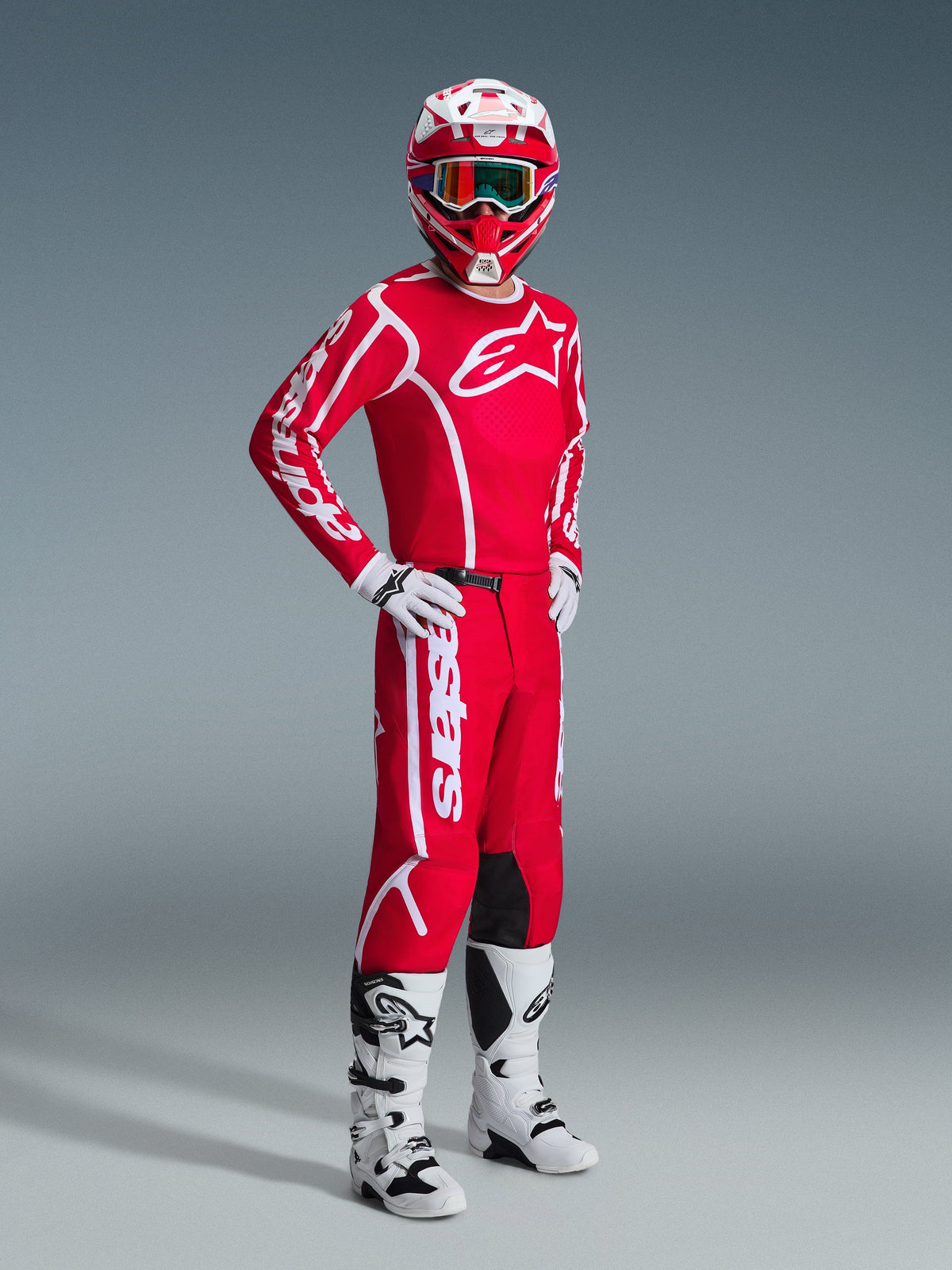 Piloto de motocross con equipamiento completo de Alpinestars, con el Jersey Fluid Apex 2026 en rojo y blanco, pantalones rojos a juego con logotipos blancos, casco rojo y blanco con gafas, botas de motocross blancas y negras, y guantes blancos, fotografía de estudio profesional de equipamiento off-road