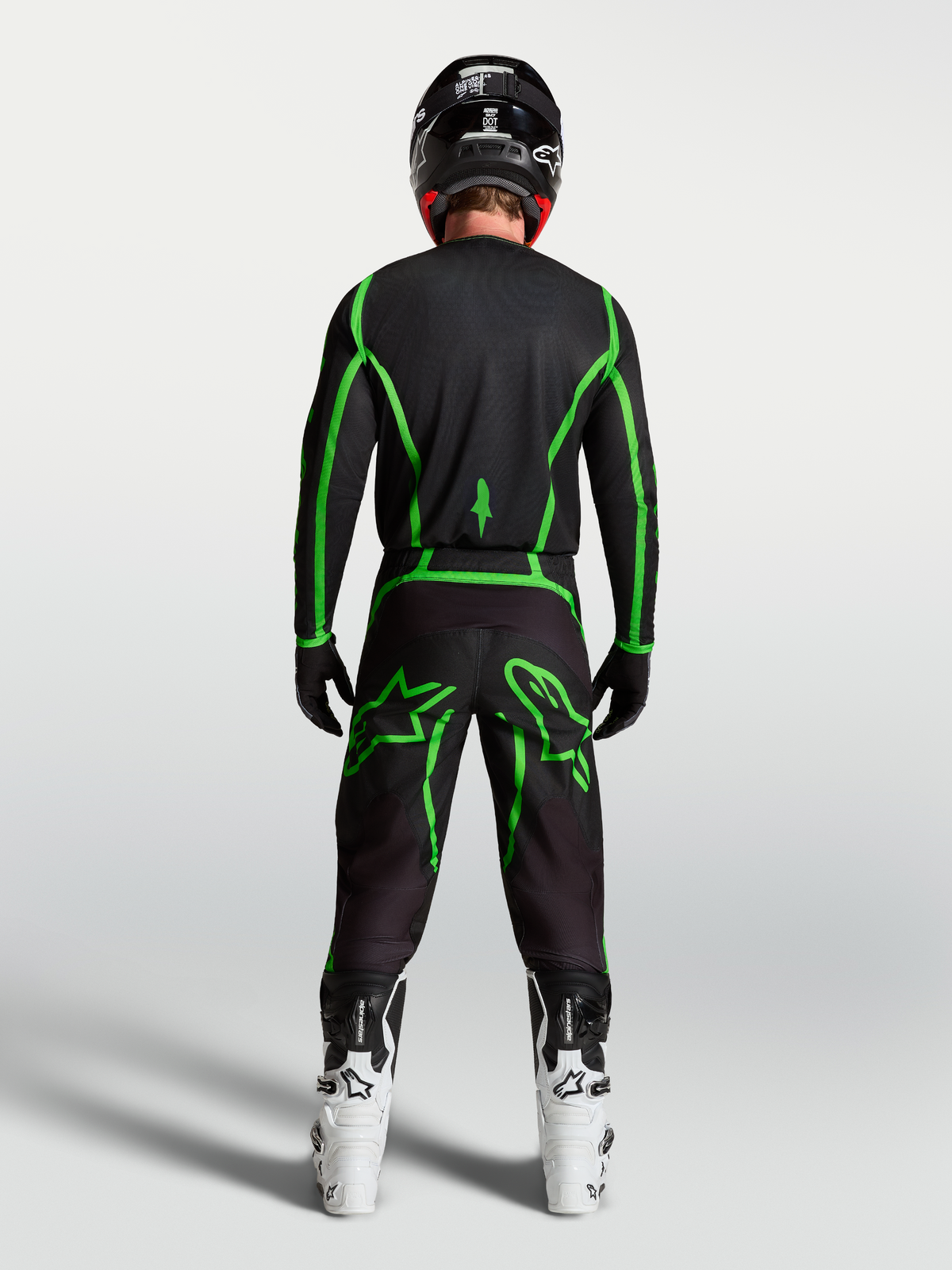 Jersey Fluid Apex V2 de Alpinestars, jersey de motocross, negro y verde fluorescente, vista trasera con botas blancas.