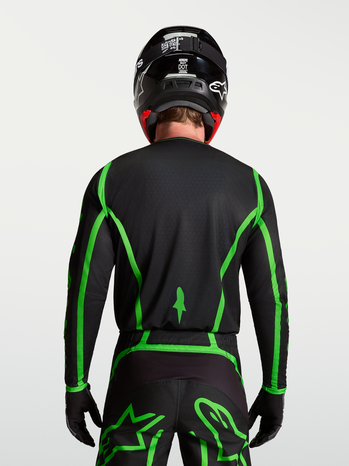 Alpinestars Jersey Fluid Apex V2, jersey de motocross, negro y verde fluorescente, vista trasera en modelo con cobertura trasera extendida para conducción off-road, diseño ligero y transpirable