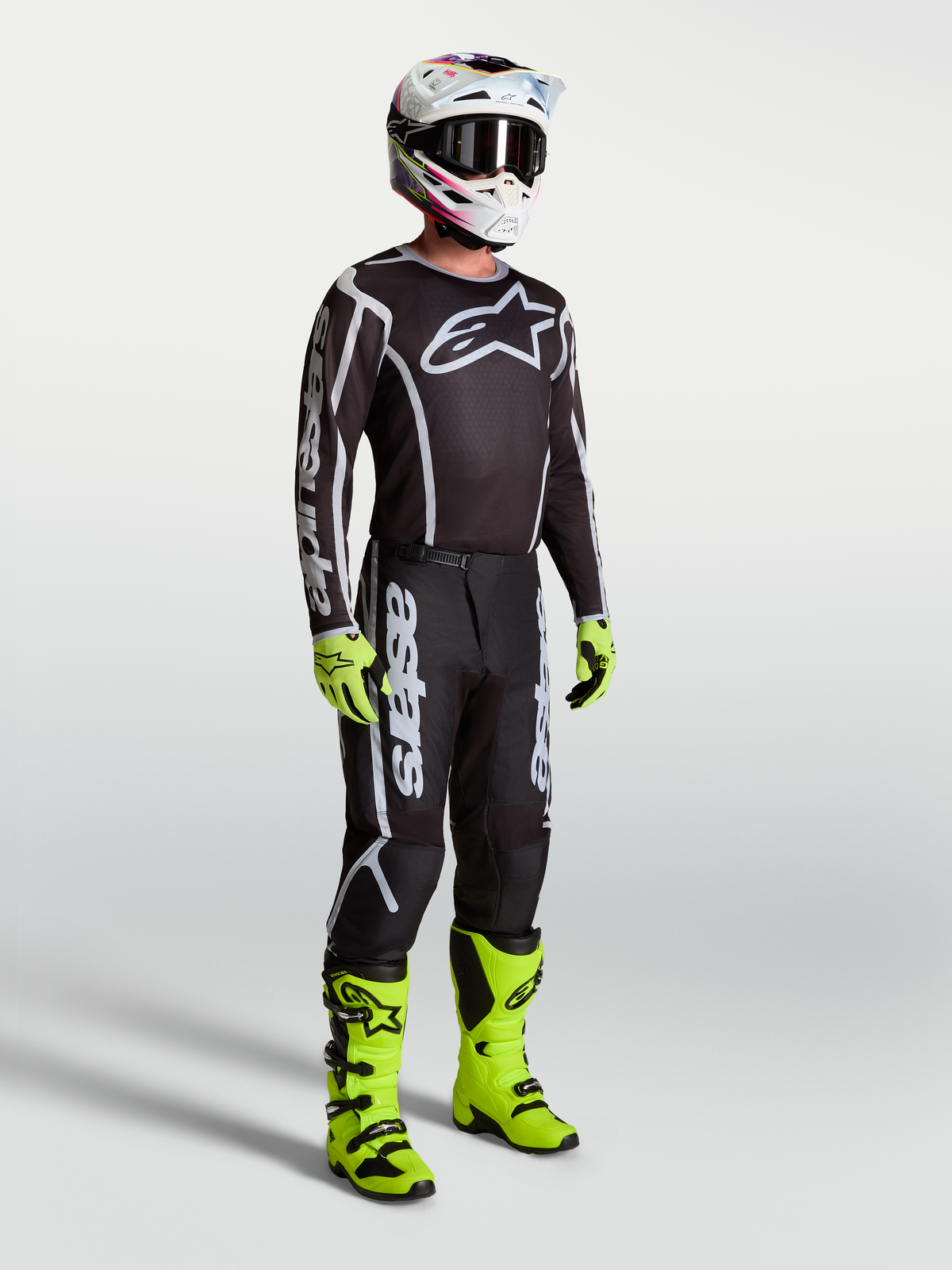 Jersey Fluid Apex V2 de Alpinestars, ropa de motocross negra y plateada en modelo con botas y guantes verdes neón.