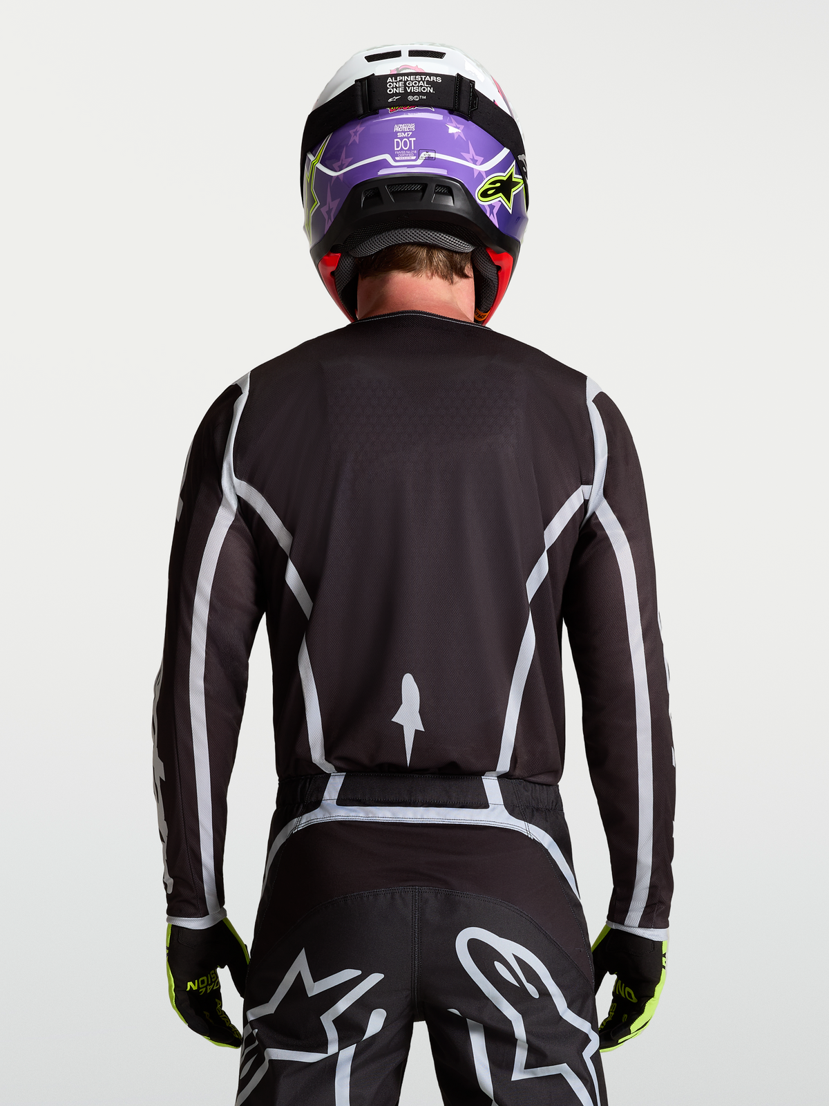 Jersey Fluid Apex V2 de Alpinestars, jersey de motocross para hombre, negro y plateado, vista trasera en modelo con ajuste atlético ergonómico.