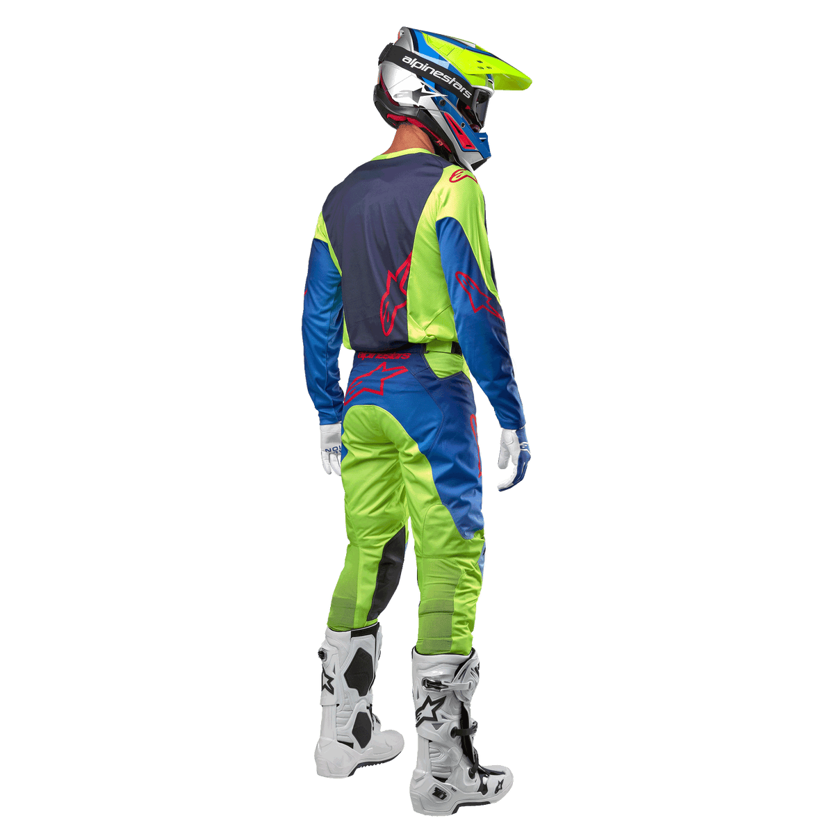 Piloto de motocross visto desde atrás con el jersey Alpinestars Racer Hoen 2024 en amarillo flúor y azul marino, pantalones de motocross a juego y botas blancas, mostrando el diseño posterior con logotipos rojos, equipamiento coordinado para conducción off-road profesional