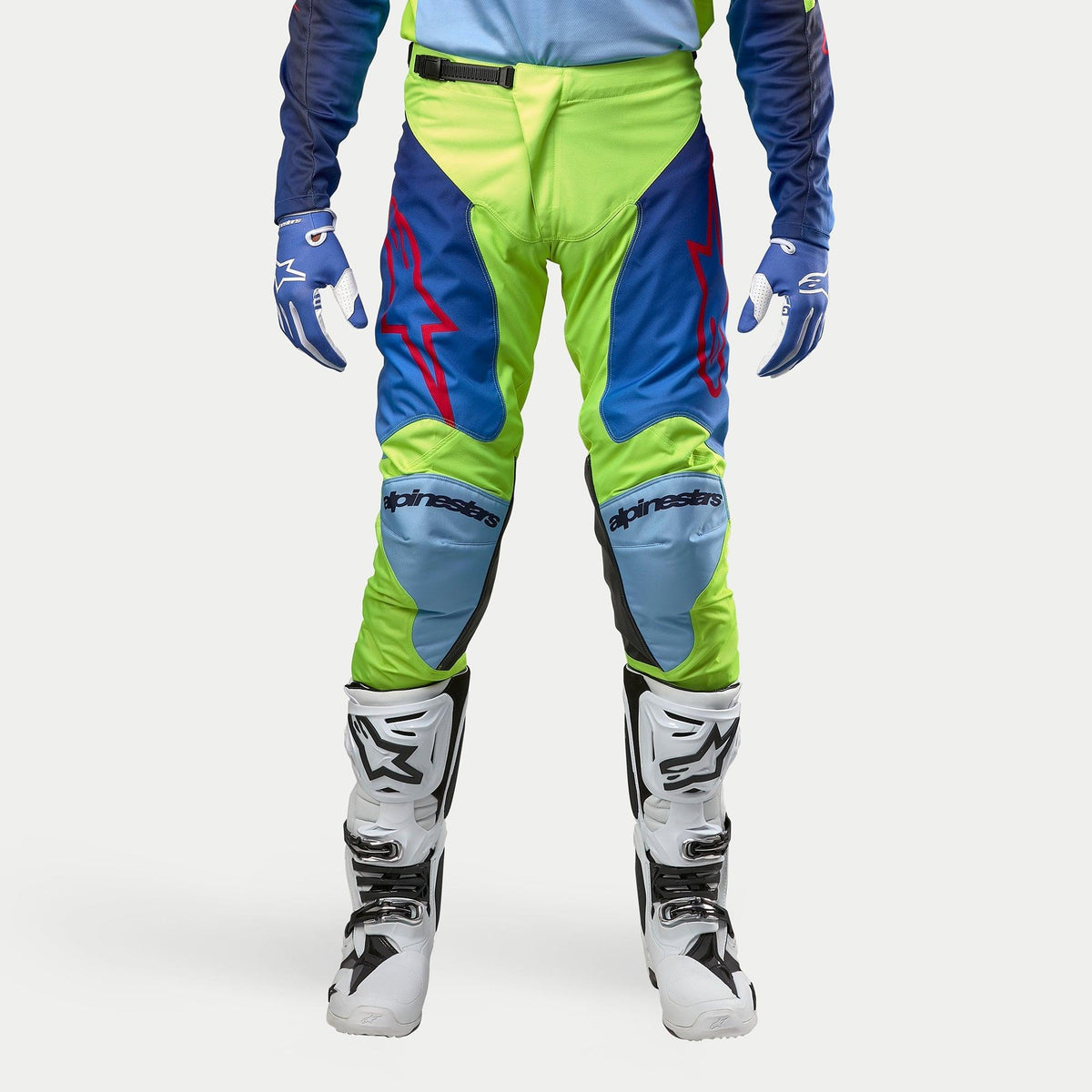 Pantalones Alpinestars Racer Hoen 2024, pantalones de motocross, color amarillo flúor y azul noche, combinados con botas de motocross blancas y negras y guantes azules, con logotipos rojos llamativos, paneles de rodilla en azul claro y un diseño ergonómico deportivo para conducción fuera de carretera