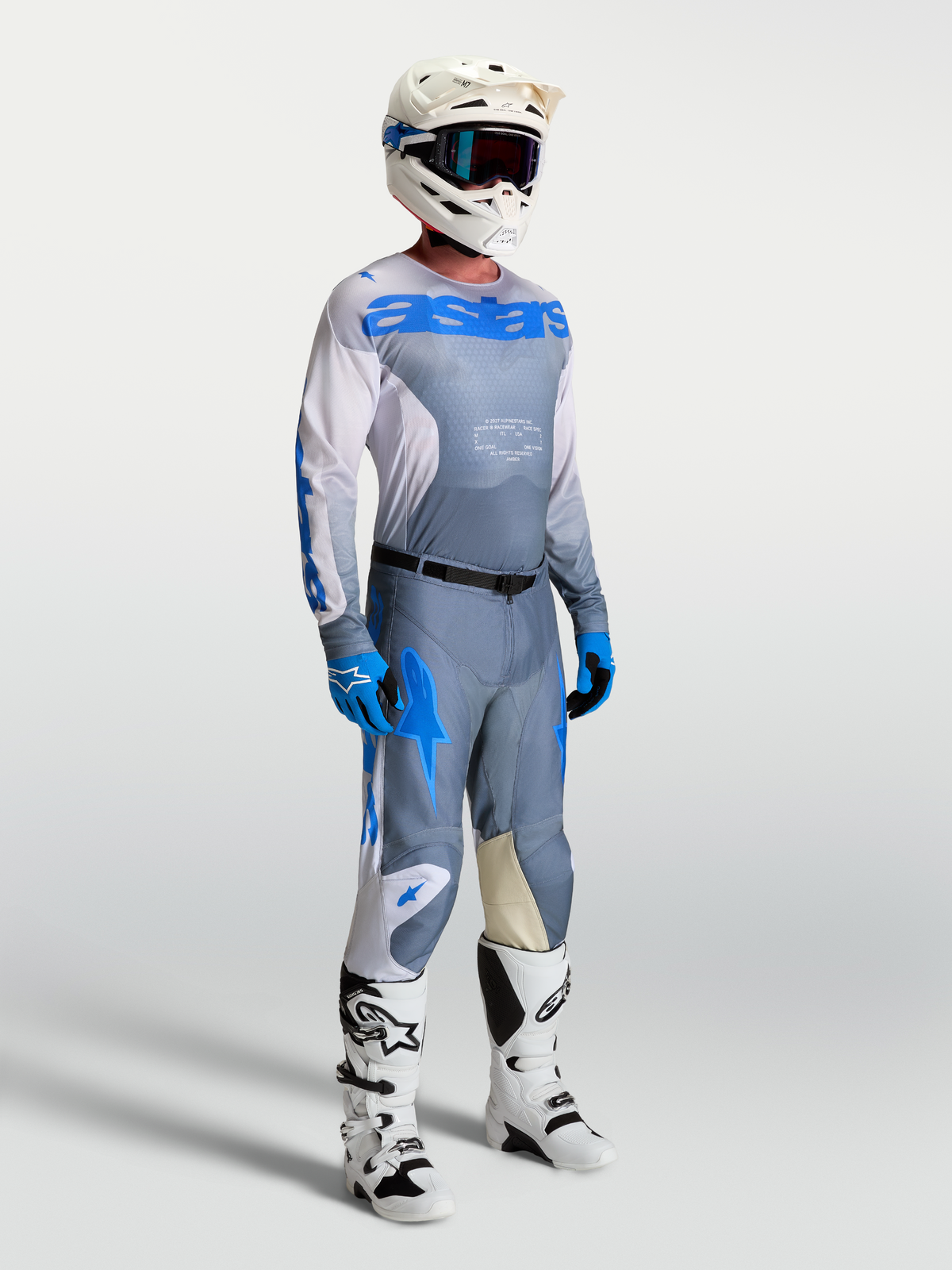 Jersey Racer Amber de Alpinestars, equipo de motocross para hombre en gris ceniza y azul UCLA, mostrado en modelo con casco y botas técnicas.