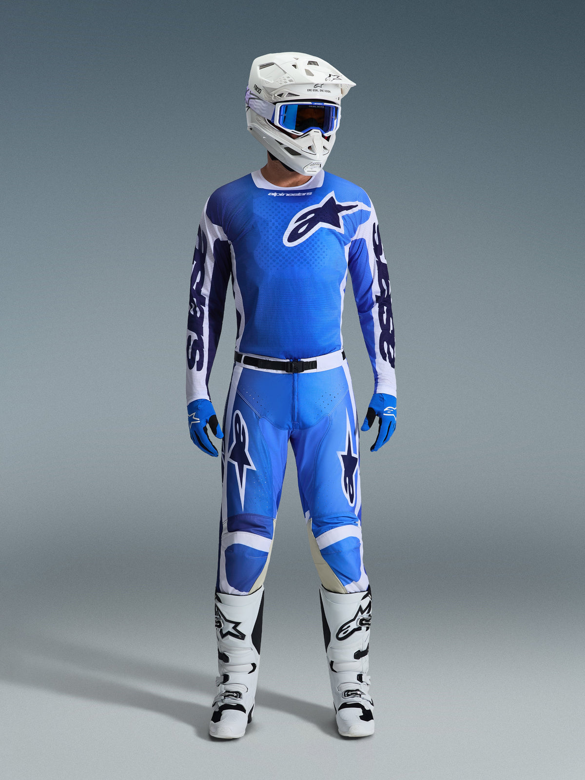 Piloto de motocross con el Jersey Alpinestars 2026 Racer Air Portl en Ucla Blue White, pantalones de motocross azules a juego, casco blanco con gafas azules, guantes azules y botas blancas, conjunto completo de equipamiento profesional para competición off-road