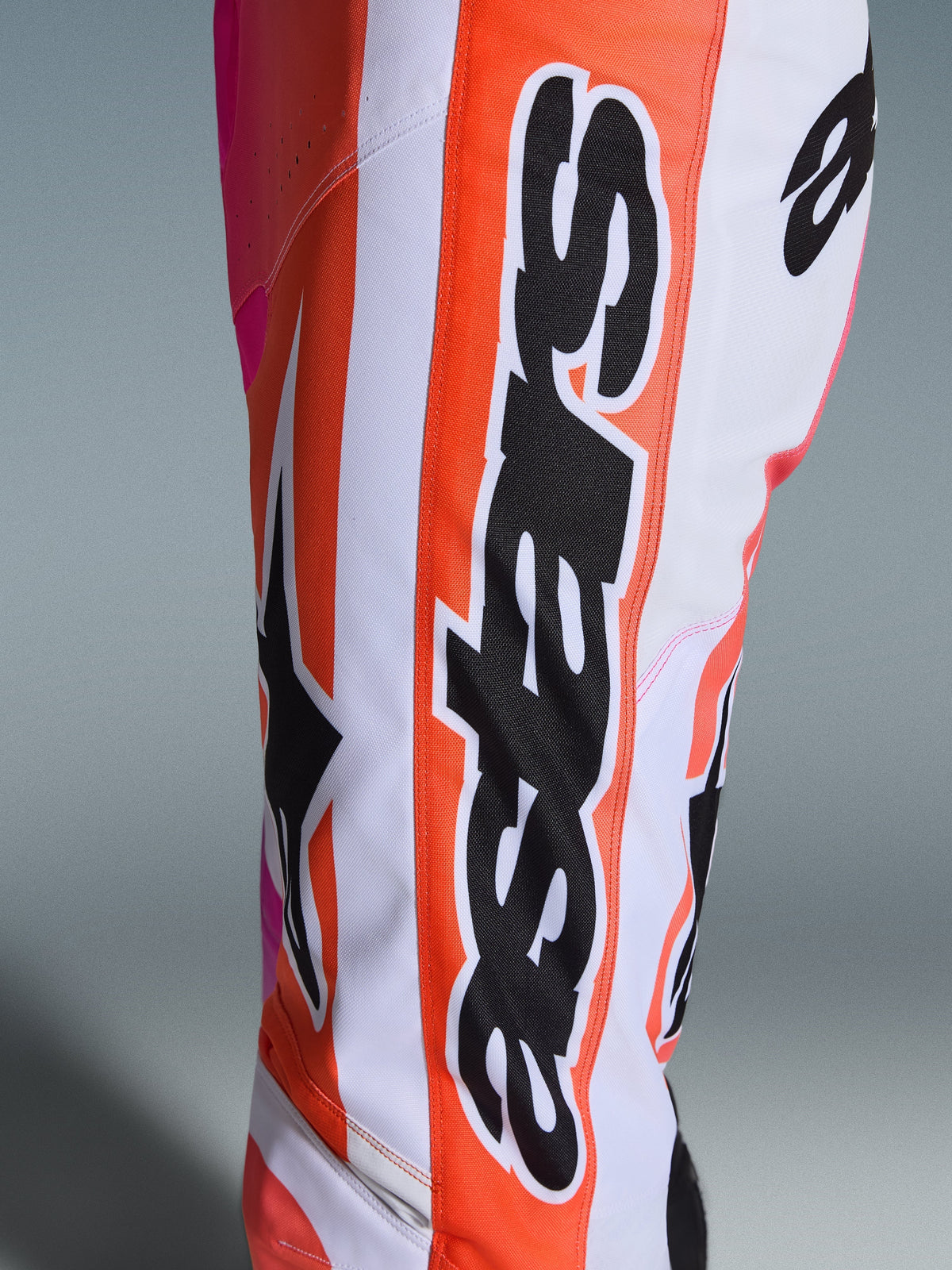 Pantalones Alpinestars Racer Air Portl 2026, pantalones de motocross en blanco, naranja y rosa, detalle de la pierna con marca vertical Alpinestars en negro sobre una franja naranja, logotipo grande de Astars y tejido perforado transpirable