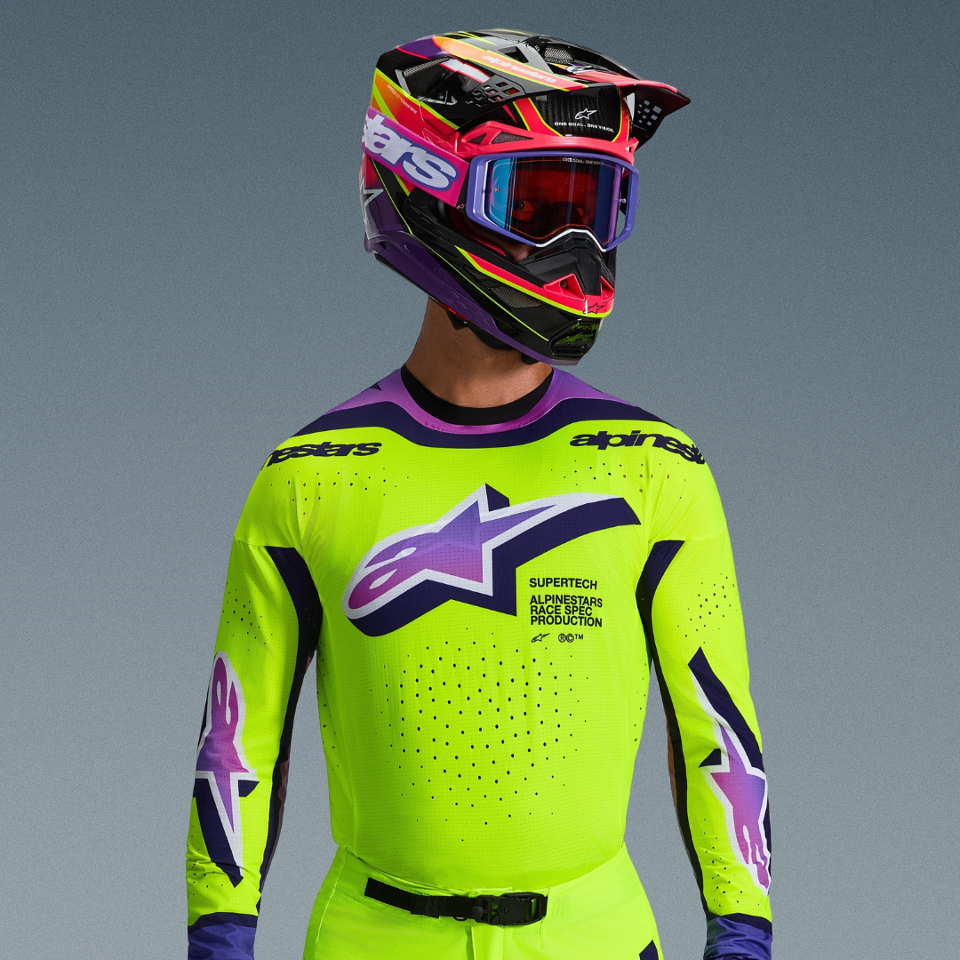Piloto de motocross con equipamiento Alpinestars Supertech Vista 2026, jersey amarillo neón con detalles morados y negros, gran logotipo morado degradado en el pecho, casco multicolor vibrante y gafas moradas a juego, con ventilación cortada con láser y ajuste atlético profesional
