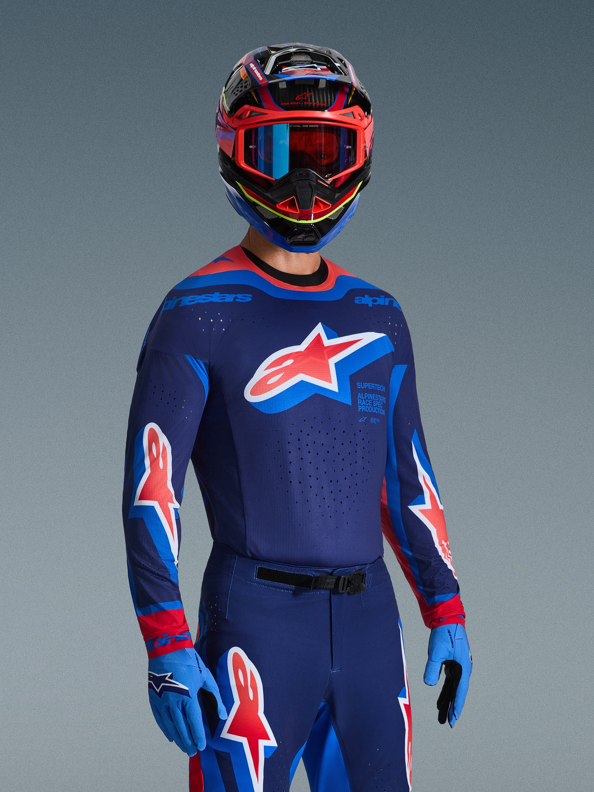 Piloto de motocross con el Jersey Supertech Vista 2026 en azul marino oscuro, coral intenso y cobalto, pantalones y guantes a juego, casco multicolor con gafas rojas, conjunto de equipamiento profesional para carreras off-road