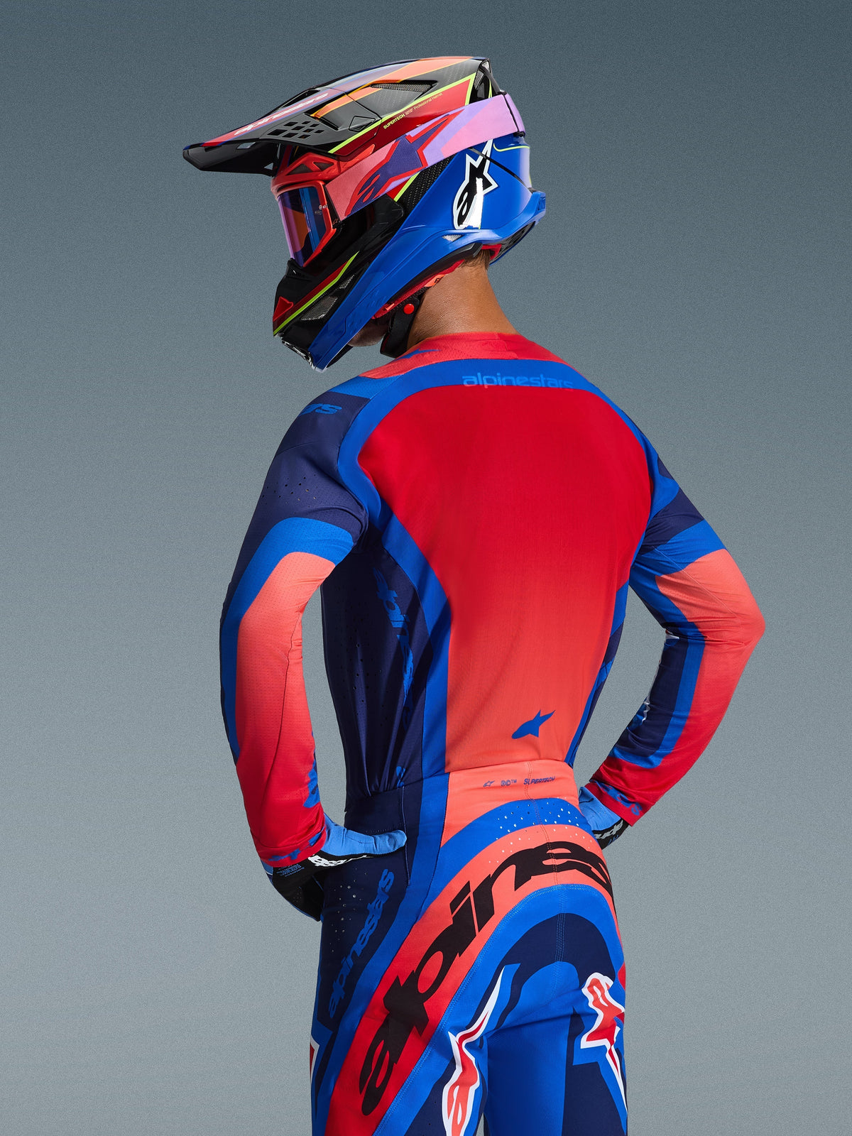 Vista trasera de un piloto de motocross con el Jersey Alpinestars Supertech Vista 2026 en Dark Navy, Hot Coral y Cobalt, con un vibrante panel trasero rojo y construcción sin costuras, combinado con pantalones y casco a juego para un look de competición completo.