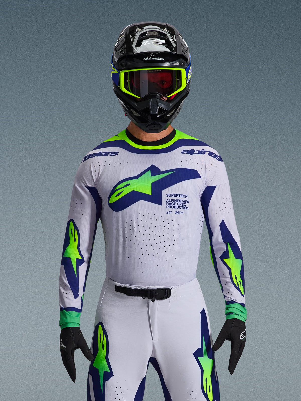 Conjunto de equipamiento Alpinestars Supertech Vista 2026, jersey y pantalones de motocross, blanco con gráficos en azul y verde neón, usado con casco negro y gafas neón, con ventilación cortada por láser y ajuste atlético de competición para carreras profesionales.