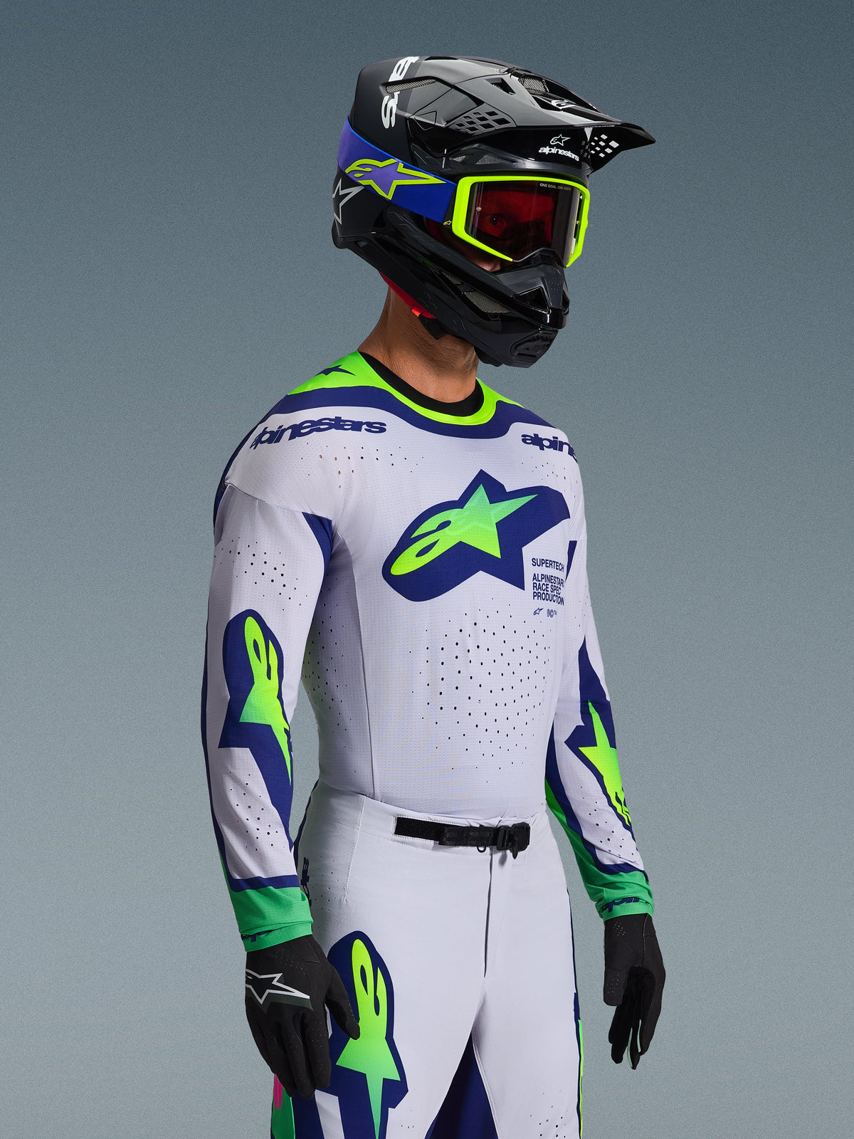 Alpinestars 2026 Supertech Vista Gear Set, jersey y pantalones de motocross, blanco con detalles en azul y verde lima, usado por un piloto con casco negro y gafas verde neón, con logotipos de estrella destacados en el pecho y las mangas, ajuste atlético de nivel profesional para rendimiento off-road.