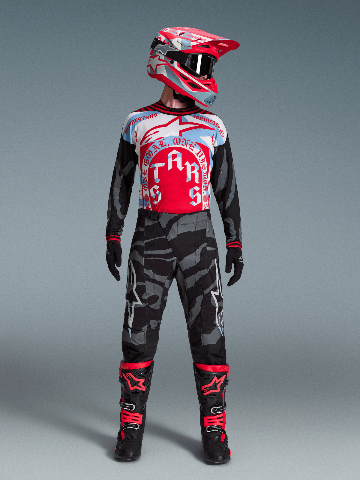 Conjunto Alpinestars Techstar Beast Coast, jersey rojo y azul, pantalones negros de camuflaje y botas de motocross.