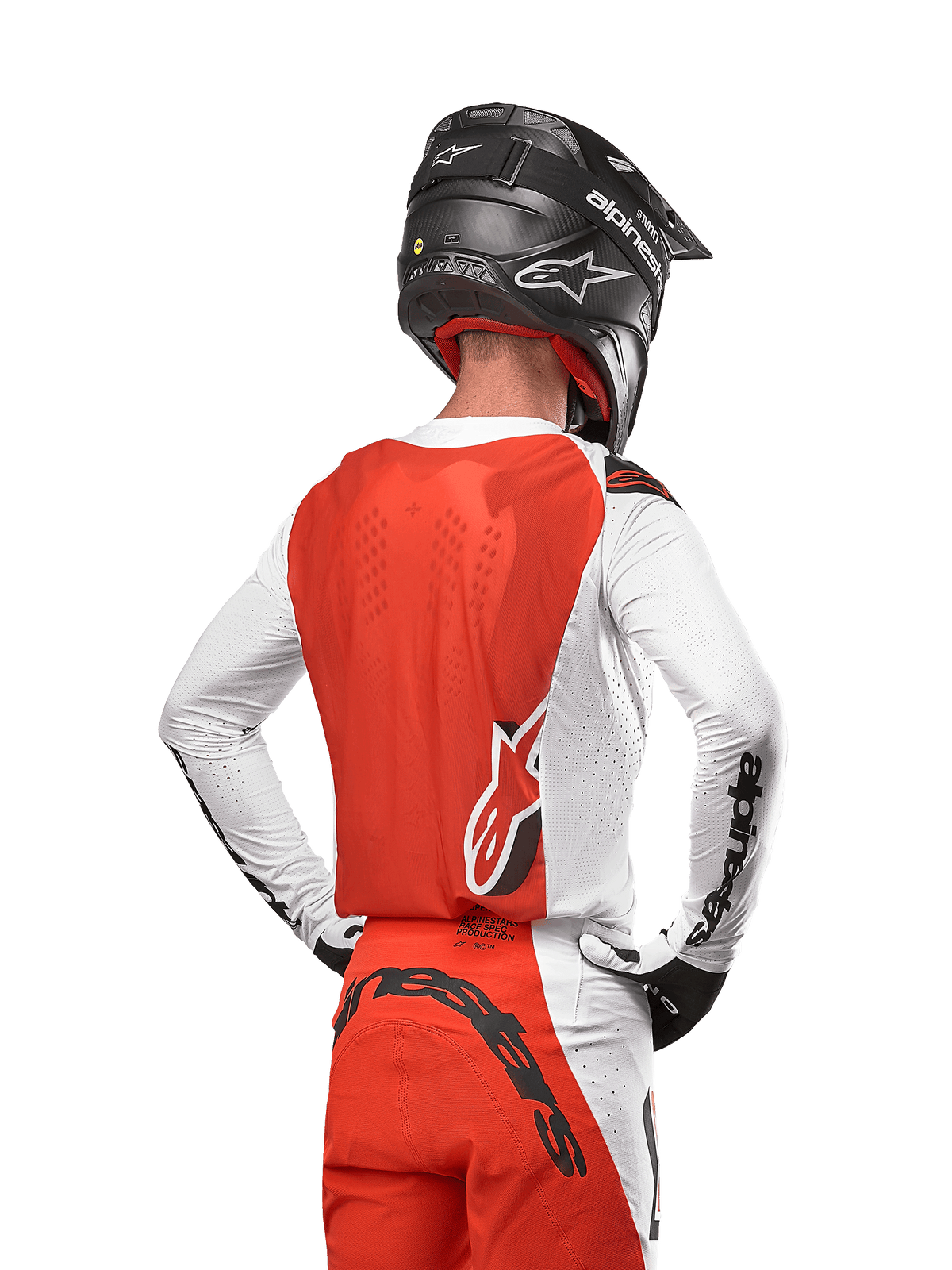 Piloto de motocross con el Jersey Alpinestars Supertech Ward 2024 en White Hot Orange, vista trasera que muestra el panel posterior naranja y mangas blancas con la marca en negro, combinado con pantalones a juego y casco negro, equipamiento profesional para carreras todoterreno