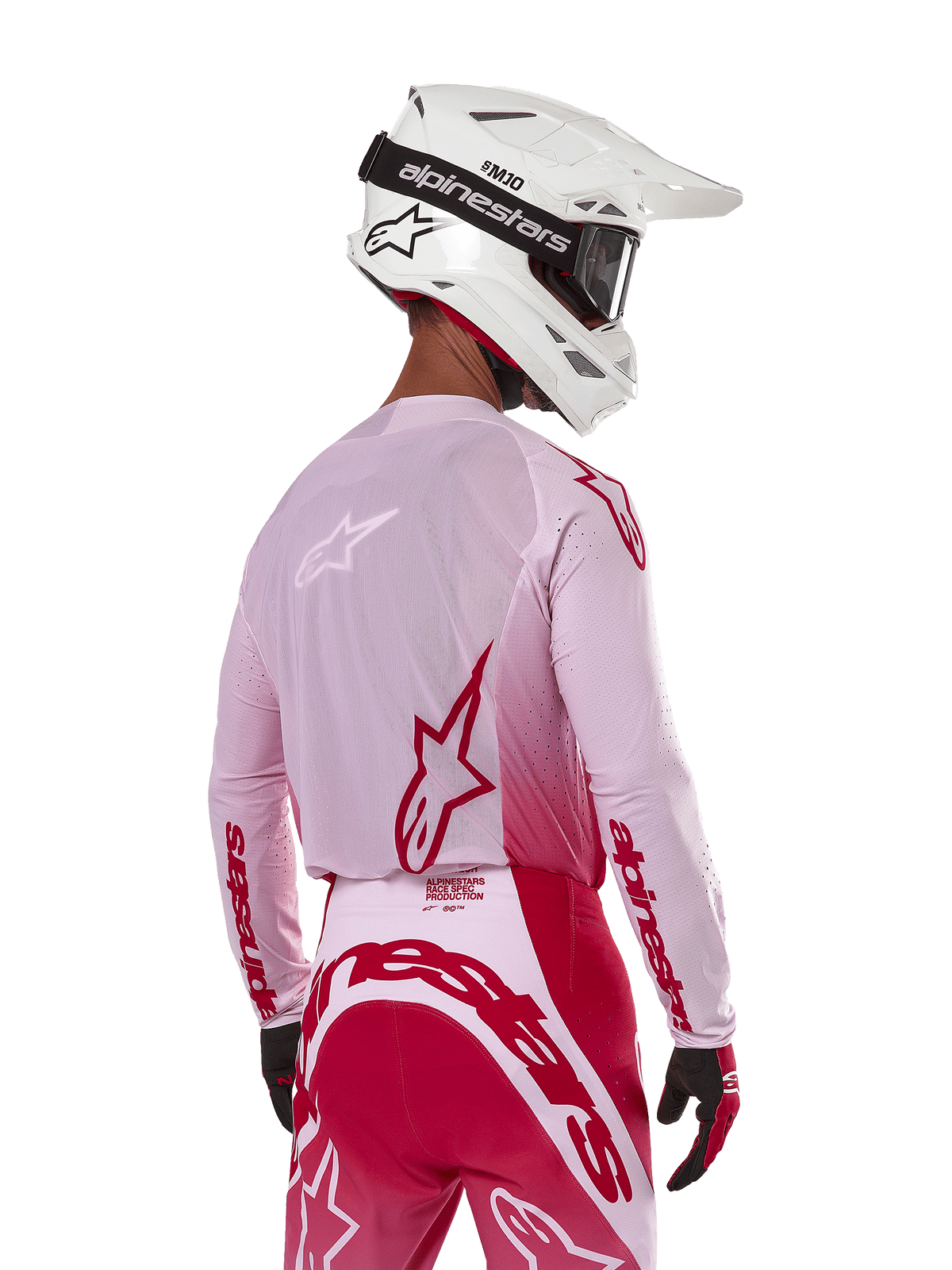 Piloto de motocross visto desde atrás con el Jersey Alpinestars 2024 Supertech Dade en Red Berry Lilac, con paneles de malla transpirable y logotipos Alpinestars en rojo, combinado con pantalones rojos y lila a juego y casco Alpinestars blanco con gafas, equipo profesional de carreras off-road