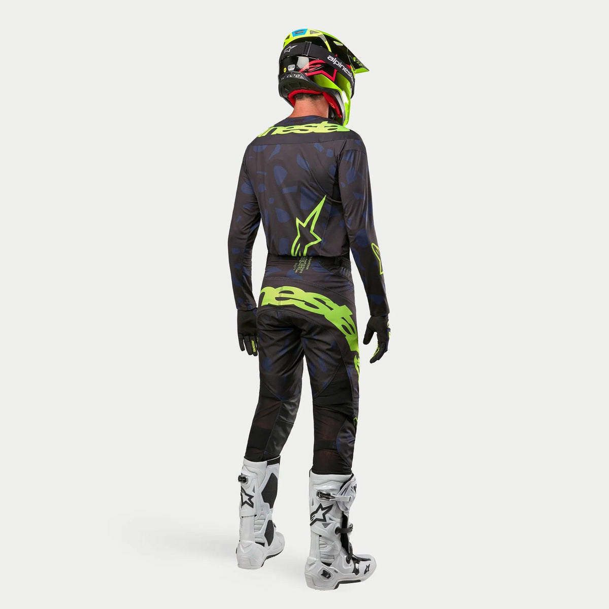 Jersey Alpinestars Techstar Rantera 2024, jersey de motocross, negro, azul marino y amarillo flúor, usado con pantalones a juego, botas blancas y negras y casco amarillo flúor, visto desde atrás con equipo completo de carreras todoterreno