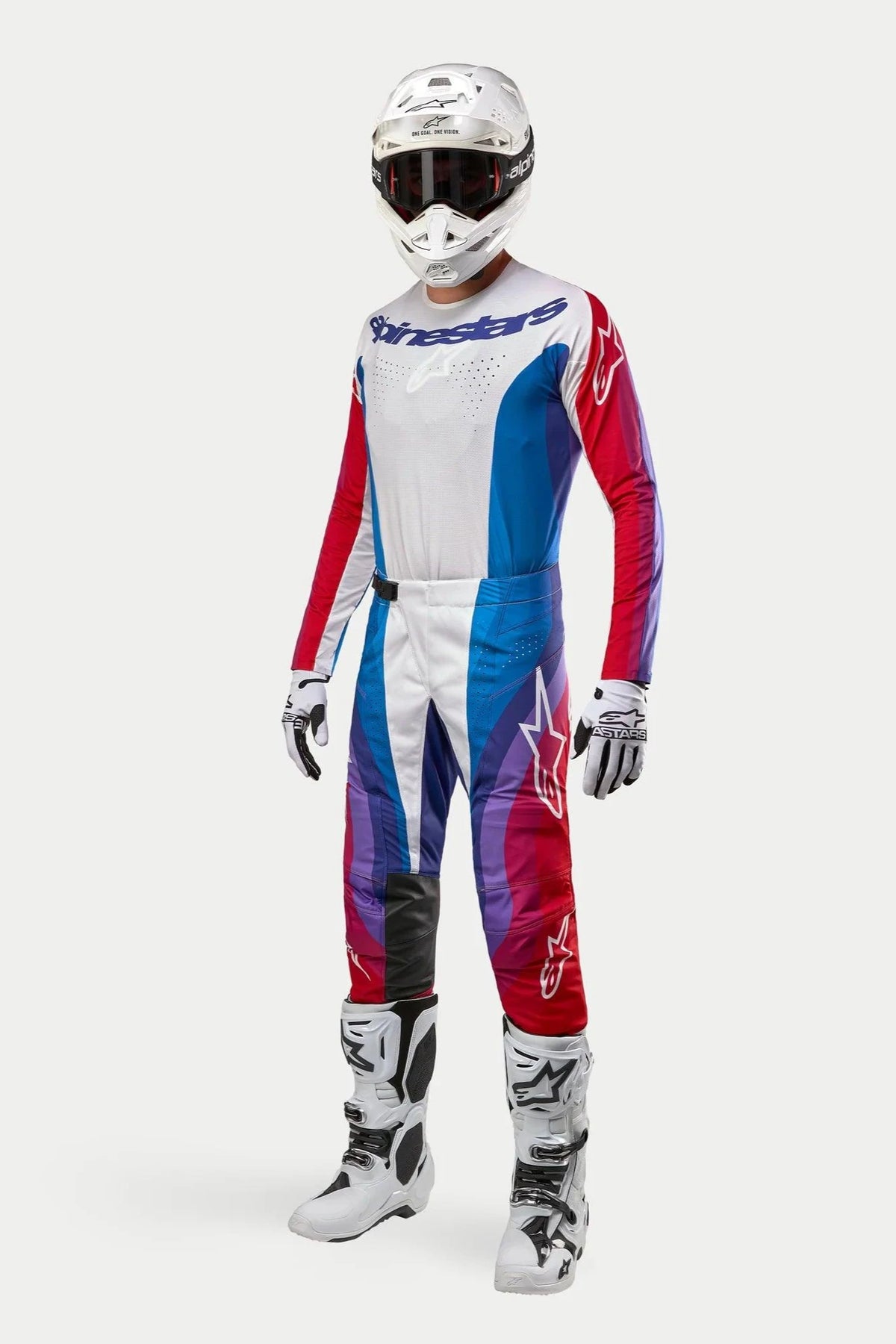 Motocross rider wearing complete Alpinestars gear, 2024 Techstar Pneuma Pants in Blue Mars Red White, matching long-sleeve jersey, white helmet with dark goggles, and white and black boots, coordinated outfit for off-road racing.