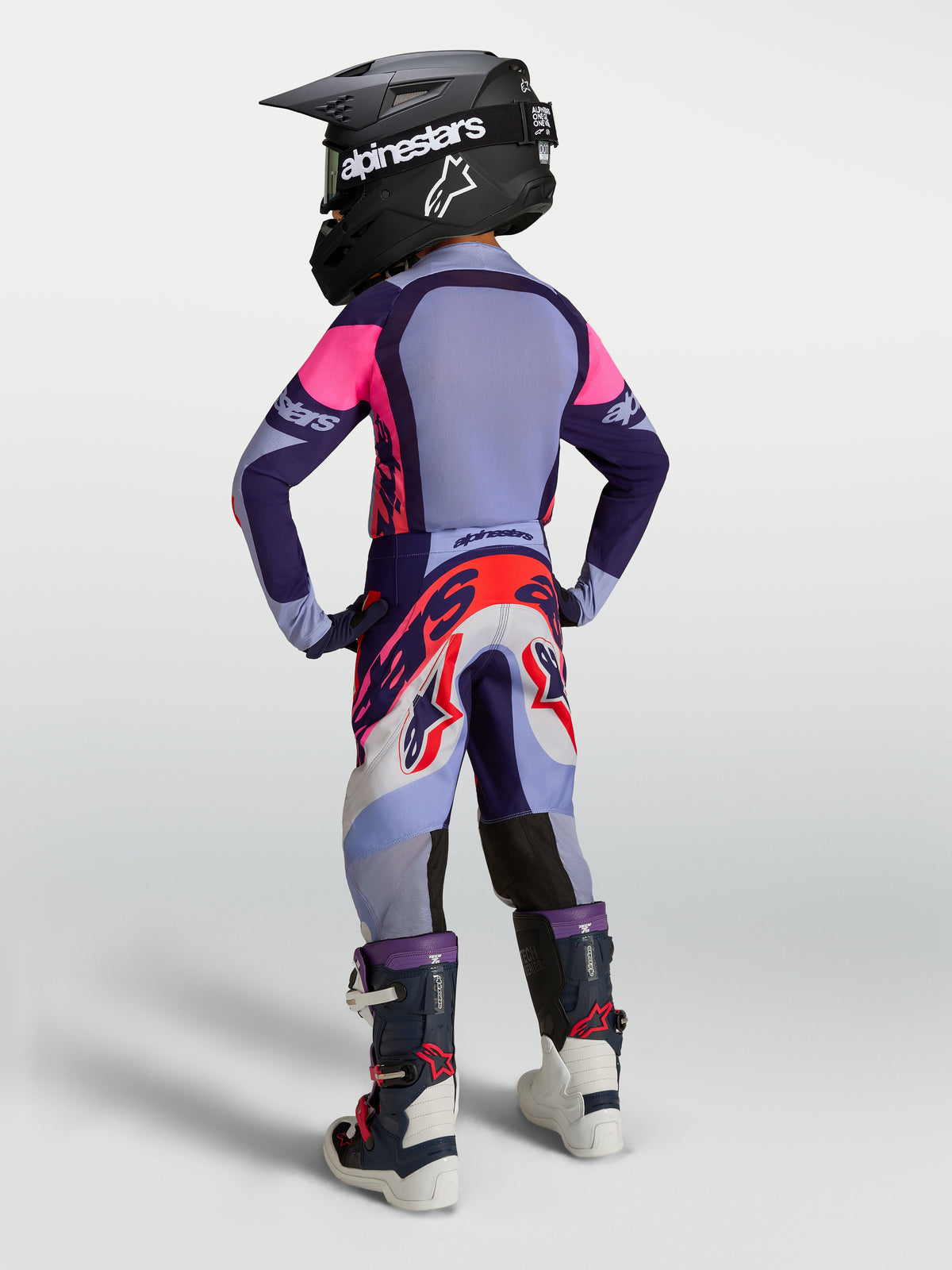 Alpinestars Supertech Dyna juvenil, conjunto de motocross morado y rosa con jersey, pantalón, botas y casco.