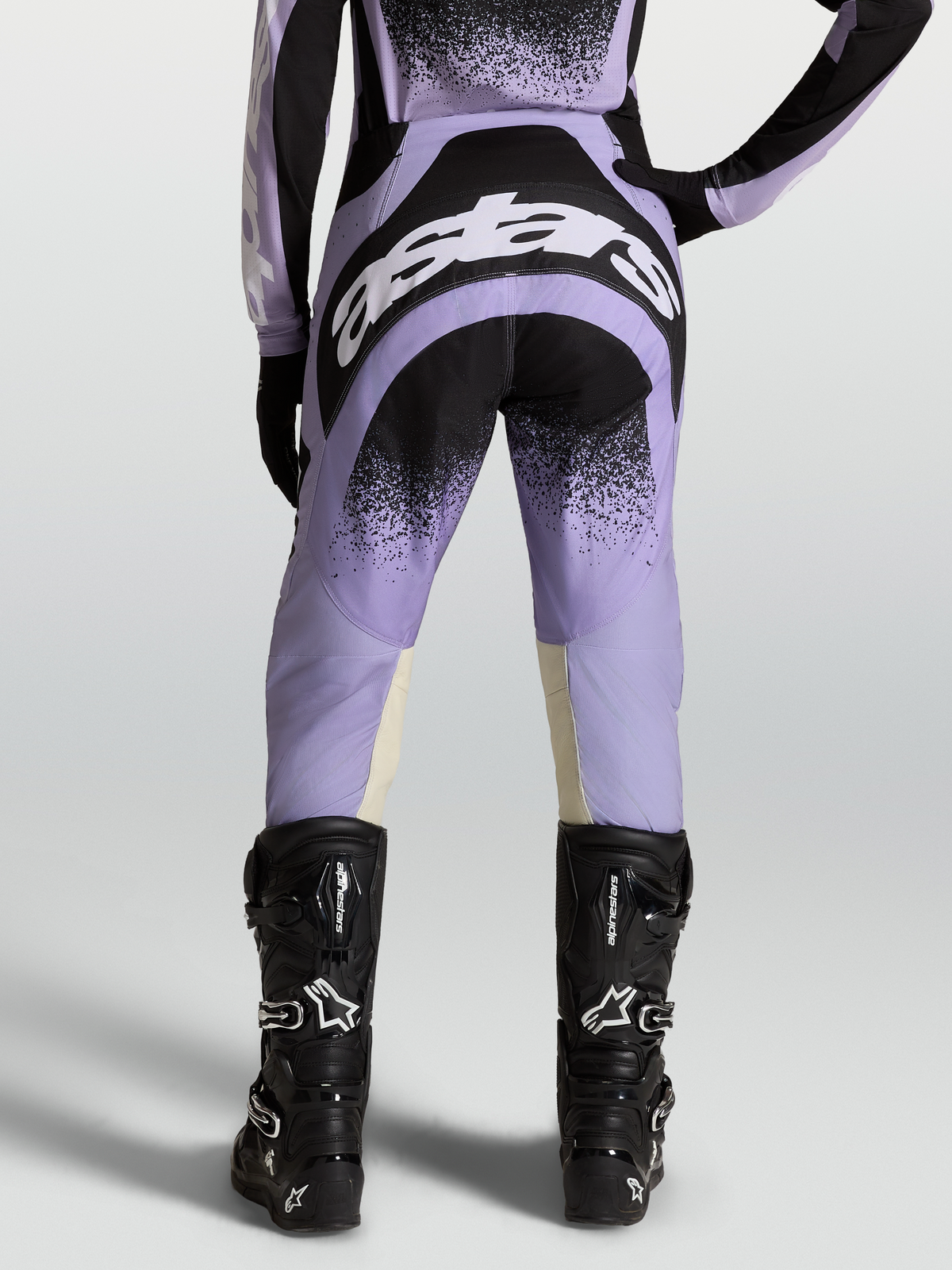 Pantalones Stella Techstar Swan, equipo de motocross para mujer, morados y negros con logotipos blancos, usados con botas negras.