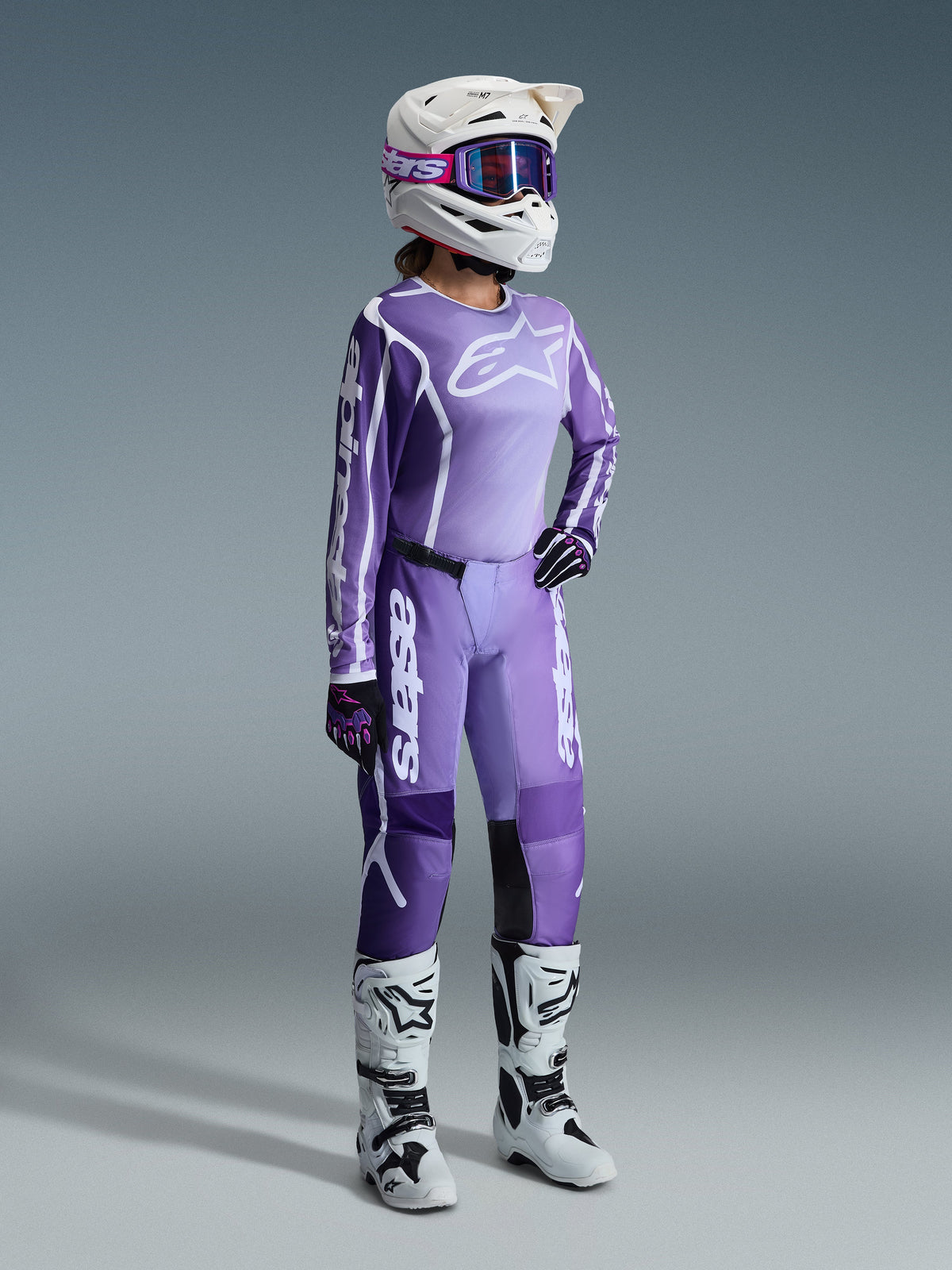Alpinestars 2026 Stella Fluid Apex Gear Set, morado y lavanda, piloto de motocross femenina con jersey y pantalones a juego, casco blanco con gafas moradas, botas blancas y negras, guantes negros y morados, equipamiento completo de alto rendimiento para carreras todoterreno de mujer