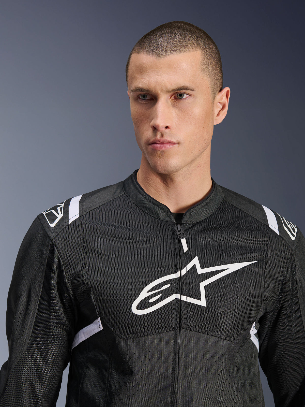 Chaqueta Alpinestars T-SPS Air V2, chaqueta de moto textil, negra y blanca, con un gran logotipo blanco en el pecho y paneles de malla, ajuste deportivo de alto rendimiento usada por un modelo masculino