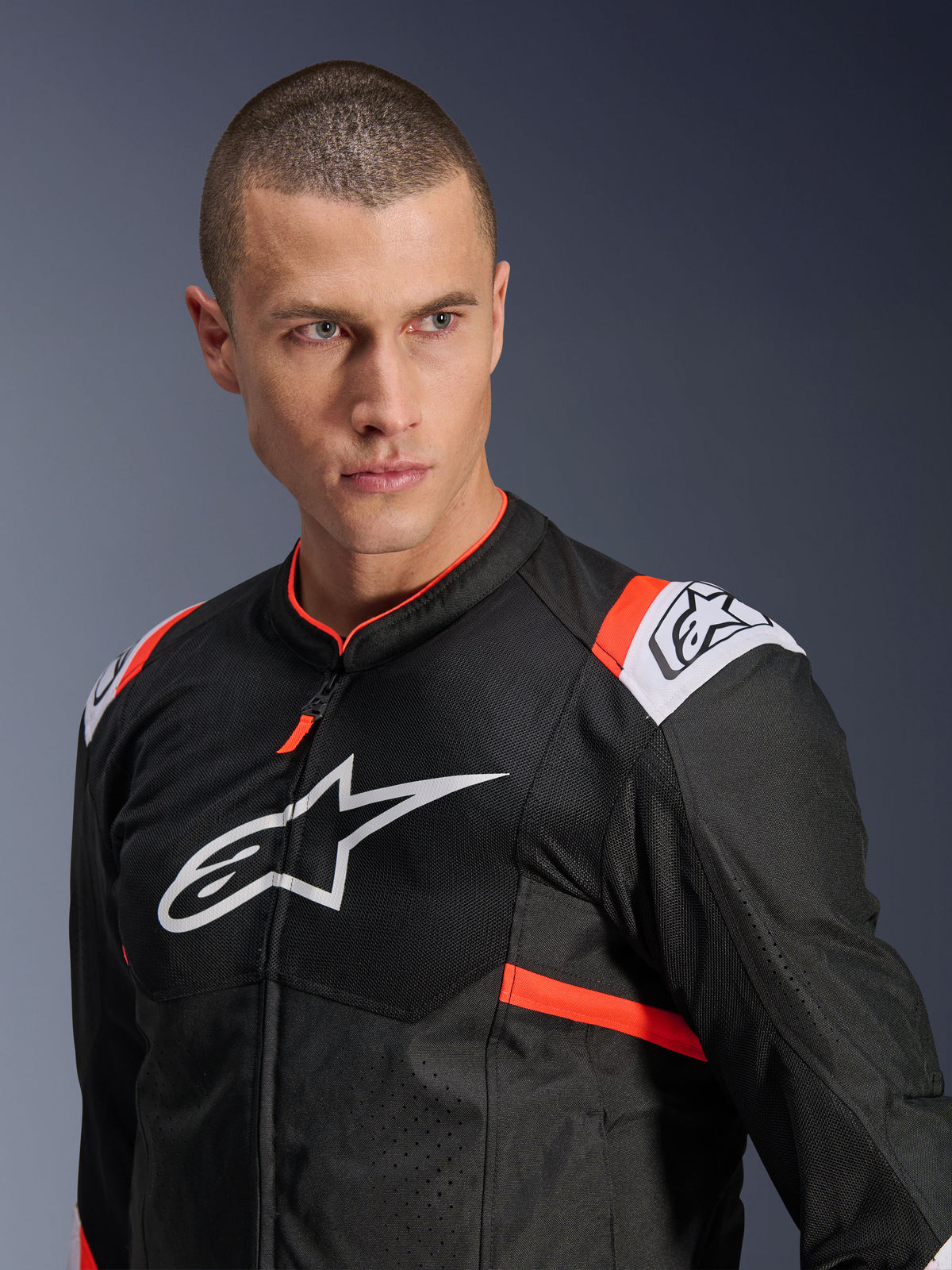 Chaqueta Alpinestars T-SPS Air v2, negra con detalles en blanco y rojo flúor, construcción de tejido de malla para flujo de aire, logotipo grande de Alpinestars en blanco en el pecho, usada por un modelo, estilo de conducción deportiva urbana