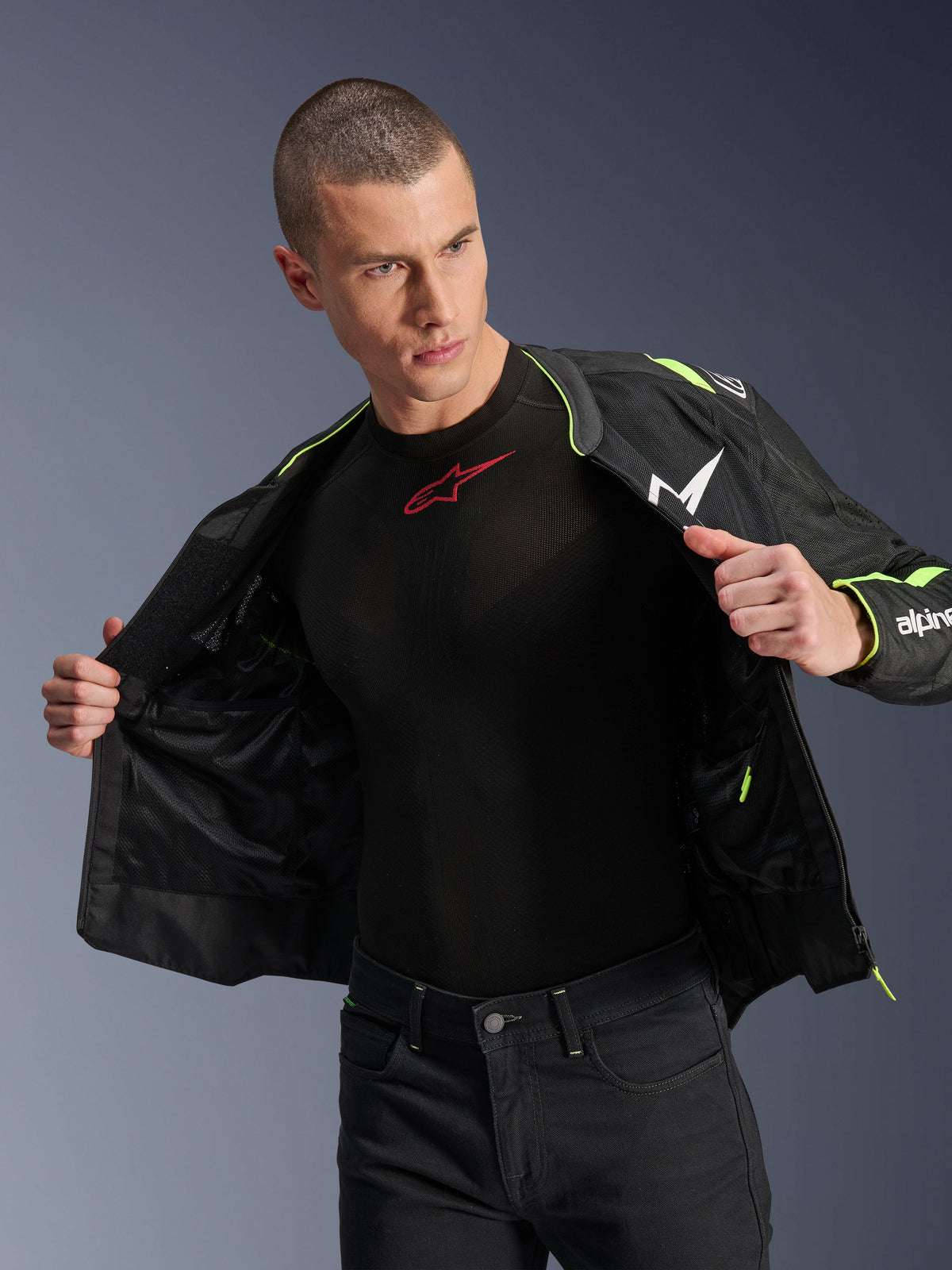 Modelo masculino vistiendo la chaqueta Alpinestars T-Sps Air V2 en negro y amarillo flúor, mostrada abierta para resaltar la construcción interna de malla y los bolsillos, combinada con una prenda técnica Alpinestars negra y pantalones negros, estilo de equipamiento urbano para motociclista