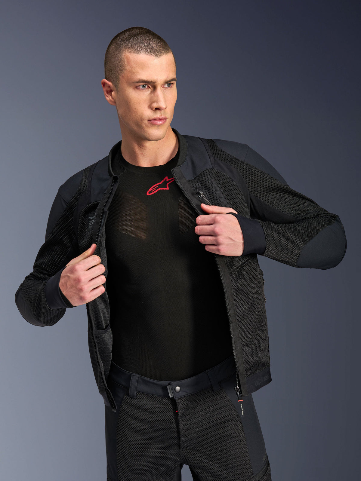 Alpinestars Troop-Air Pro Jacket, negra, chaqueta de aire técnica blindada premium con construcción de malla, usada abierta sobre una capa base negra con un logo rojo, combinada con pantalones de moto de malla a juego, estilo de conducción urbano contemporáneo