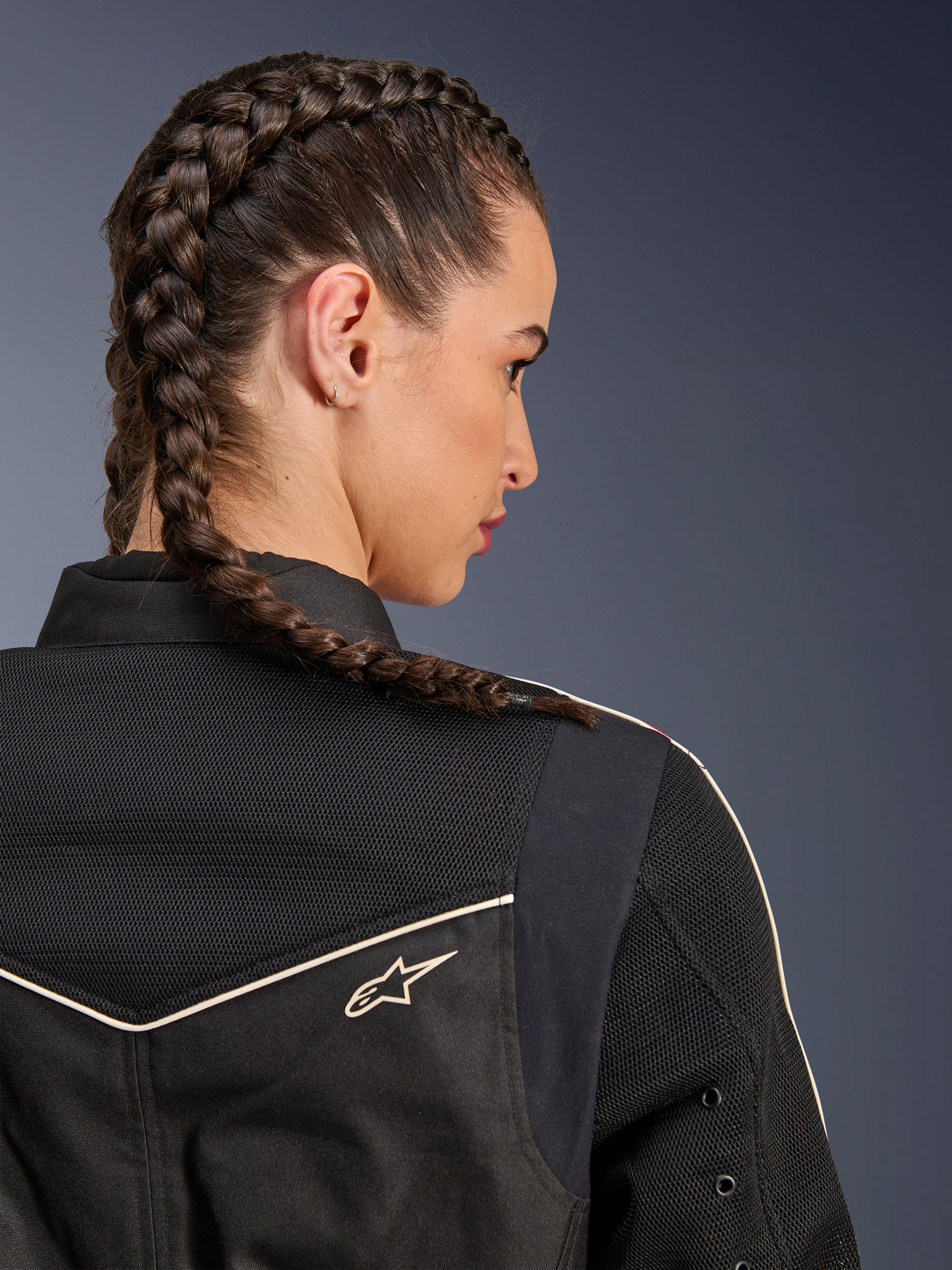 Woman wearing the Alpinestars Stella T-Dyno Air Jacket, close-up rear view focusing on the shoulders and yoke, Black with breathable 3D mesh panels, white piping and small Astars logo, model with braided hair, urban motorcycle riding apparel