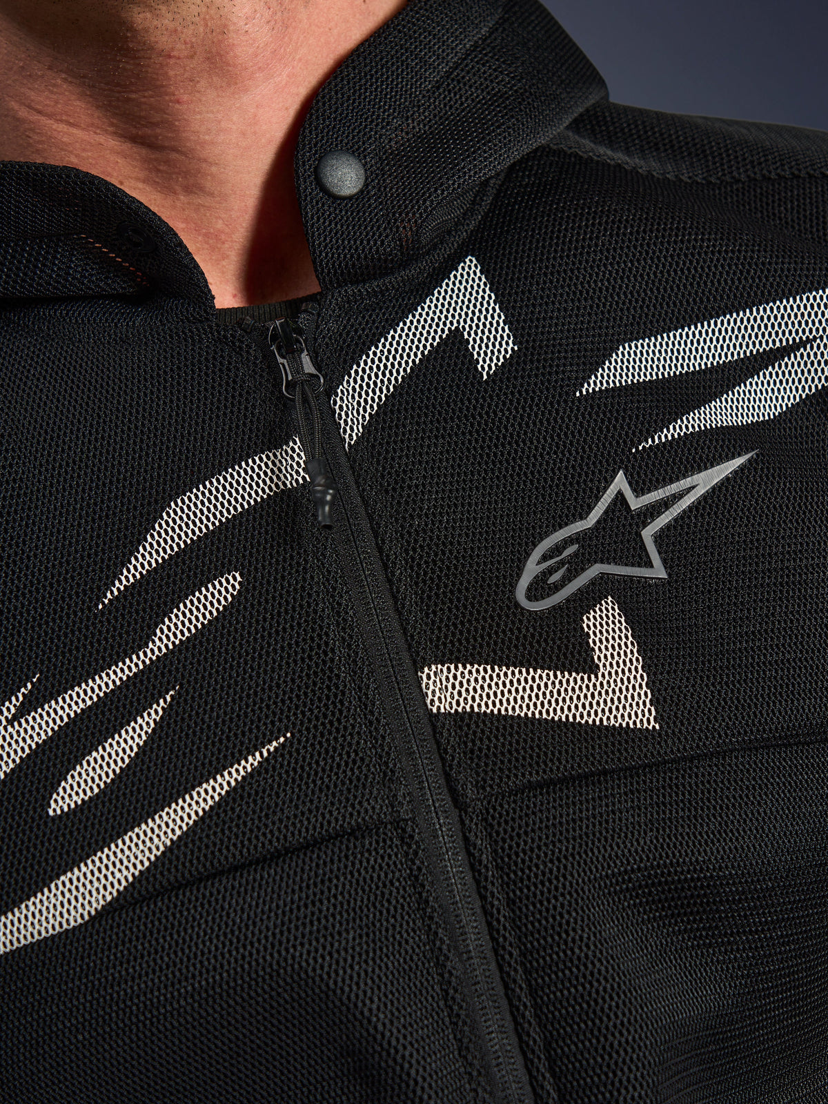 Alpinestars Chrome Superairflow Hoodie, sudadera para moto, negra con gráficos blancos y grises, primer plano del pecho mostrando la construcción de malla técnica 3D, cremallera frontal y cuello con botón a presión, con el logotipo de Alpinestars