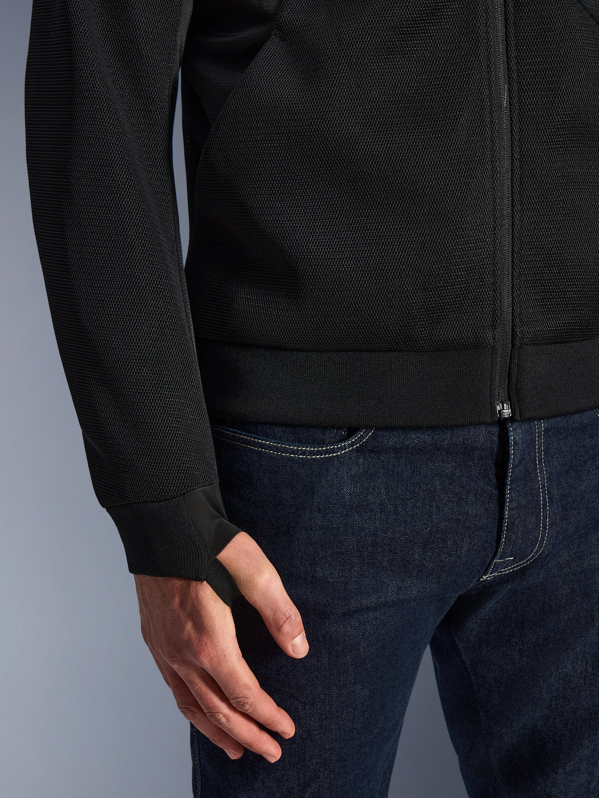 Alpinestars Chrome Superairflow Hoodie, negra, primer plano del tejido de malla técnica 3D de alta resistencia, con puño de punto jersey elástico acanalado y lazo para el pulgar, combinada con vaqueros azules
