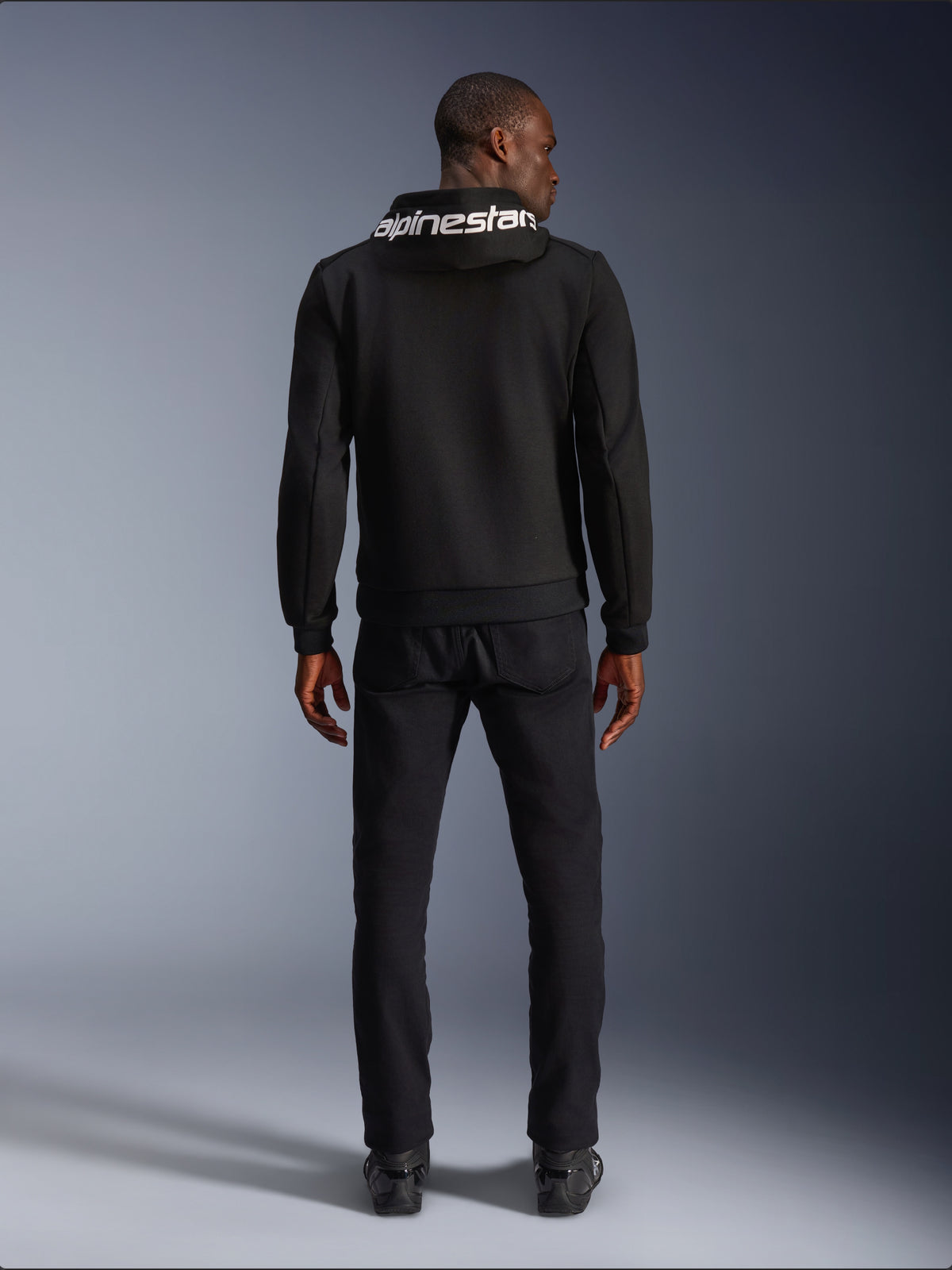 Sudadera Alpinestars Chrome V2 Sport para moto, negra con logo blanco en la capucha, vista trasera en modelo.