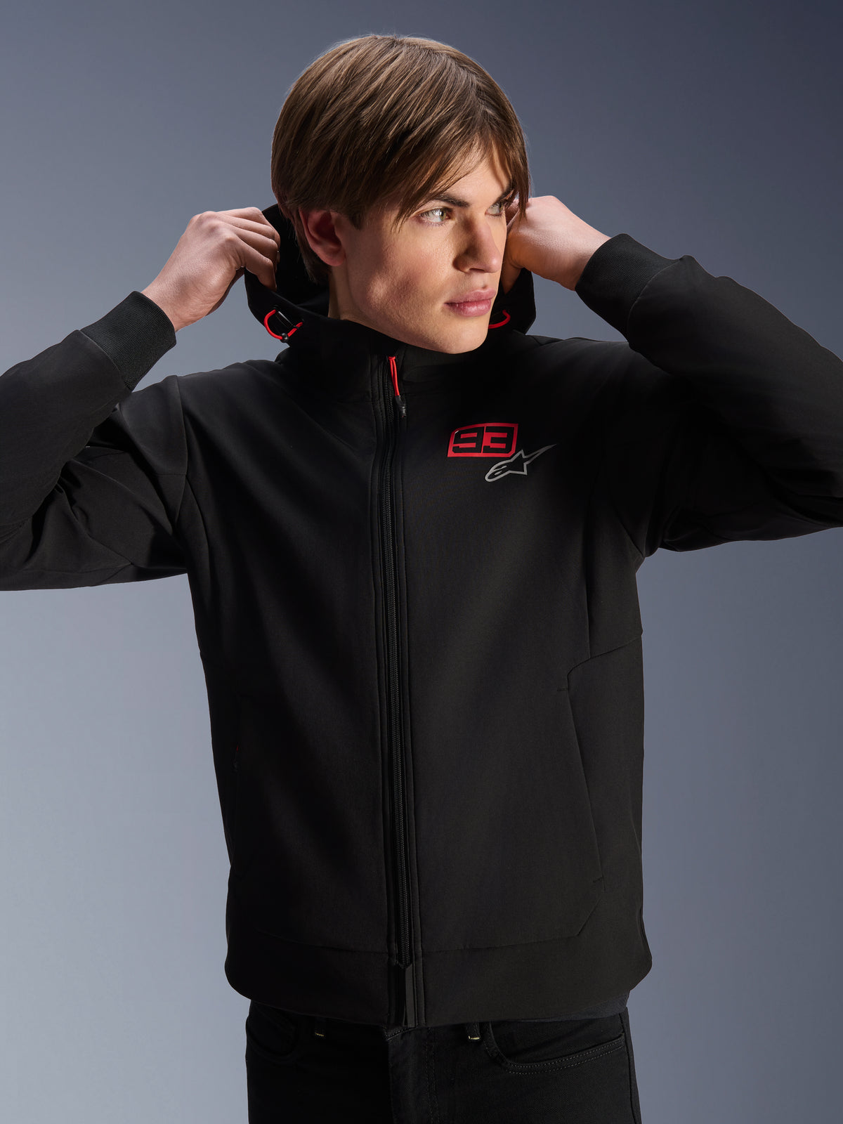 Alpinestars MM93 Radium Tech Hoodie, urban motorcycle jacket, black with red and silver logos, worn by a male model, features a full-length zipper and ribbed cuffs, casual lifestyle motorsport apparel