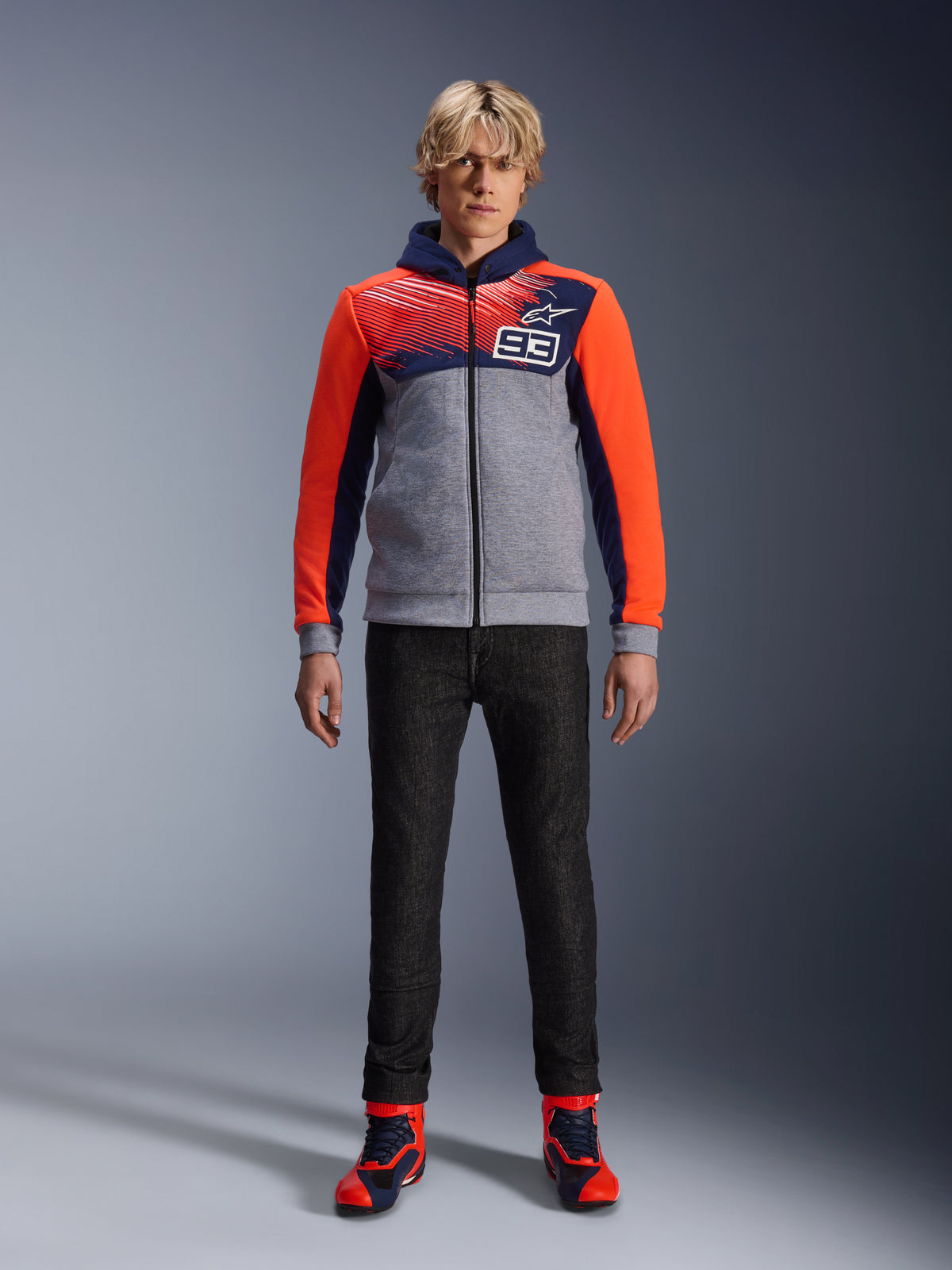 Alpinestars MM93 Chrome V2 Sport Hoodie, Motorcycle Riding Hoodie, Blue Navy Gray Melange and Red Fluo, worn with dark riding pants and red-accented sneakers, featuring a full-length zipper and MM93 logo, casual urban motorsport-inspired design