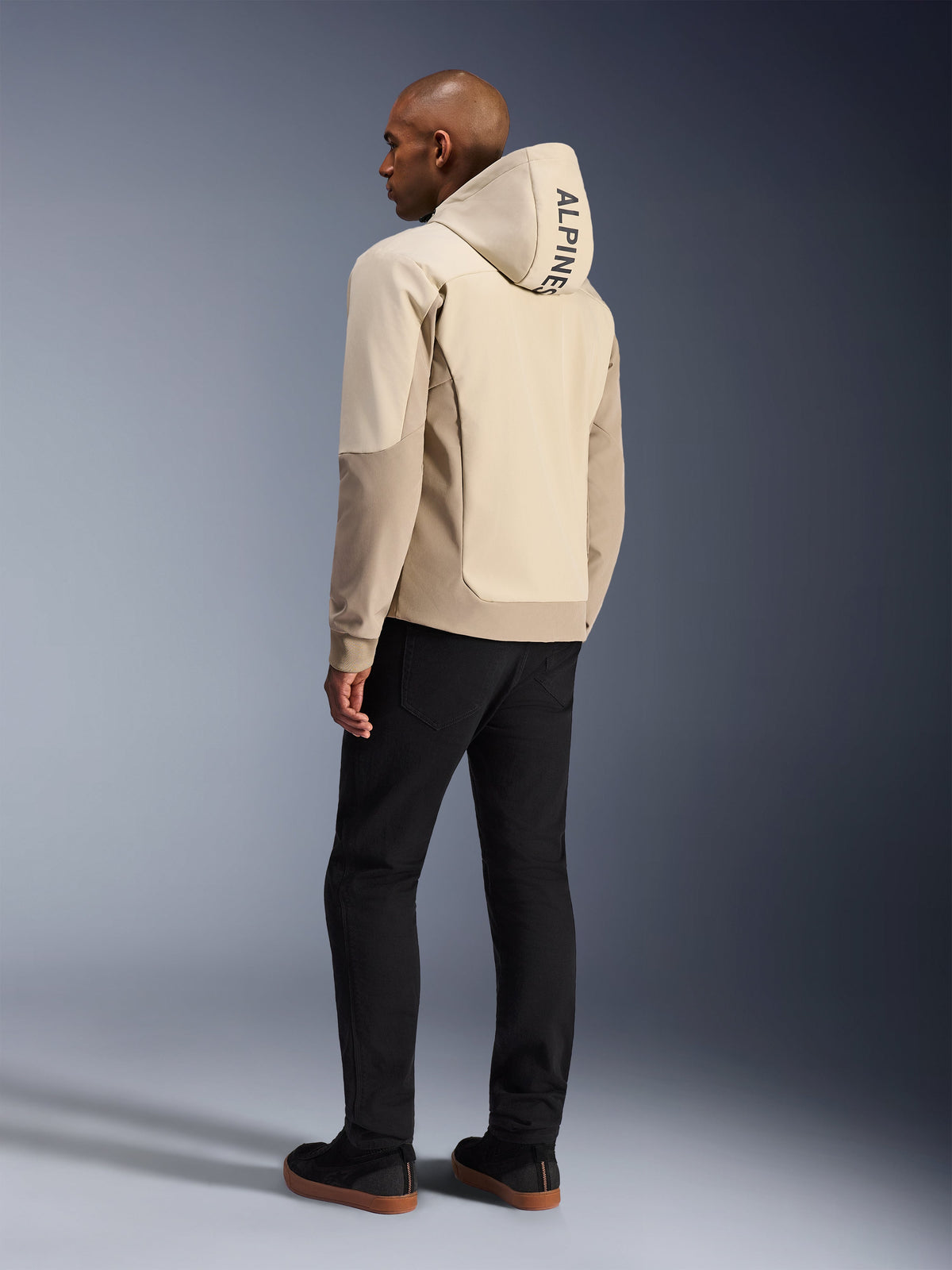 Alpinestars Radium Tech Hoodie en Mastic Aluminum, chaqueta urbana de motociclismo, vista trasera en modelo con la capucha puesta, marca vertical ALPINESTARS en la capucha, combinada con pantalones negros, construcción textil moderna para protección en conducción urbana