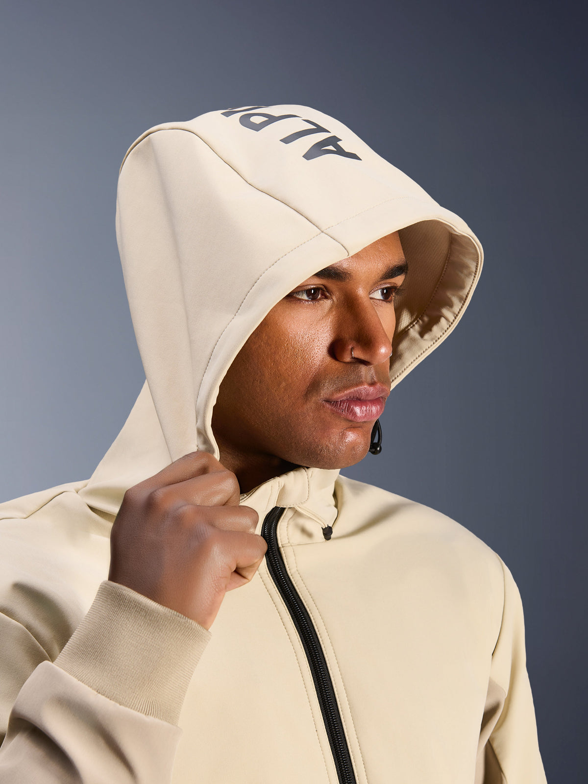 Alpinestars Radium Tech Hoodie en Mastic Aluminum, primer plano de un hombre con la capucha puesta, con el logotipo de Alpinestars en la parte superior, chaqueta de moto urbana con capa técnica cortavientos, estética streetwear moderna para conducción en ciudad