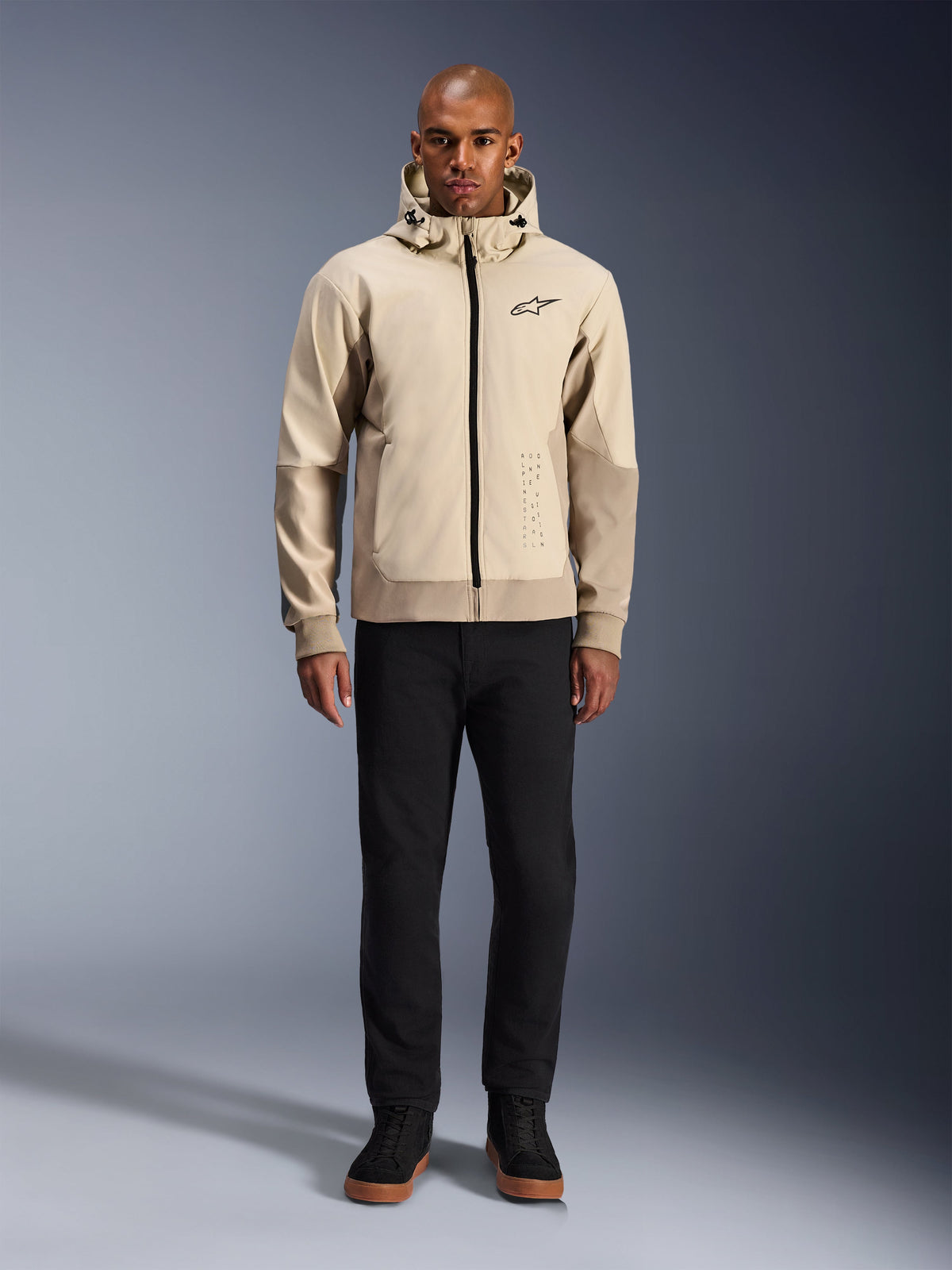 Alpinestars Radium Tech Hoodie en Mastic Aluminum, sudadera urbana para motociclista usada por un modelo masculino con pantalones y botas negras, con cremallera negra completa, logotipo pequeño en el pecho y ajuste atlético para conducción en ciudad.
