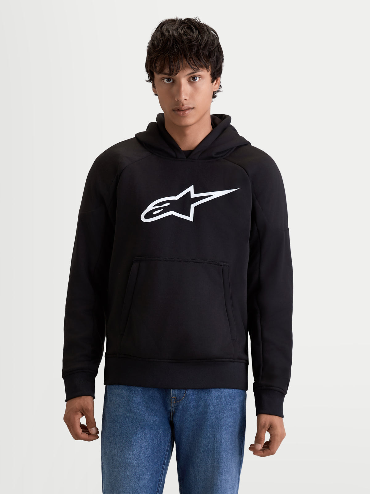 Alpinestars Ageless Hoodie, chaqueta con capucha de moto urbana para hombre en negro con logotipo blanco en el pecho y bolsillo tipo canguro, vista frontal en modelo