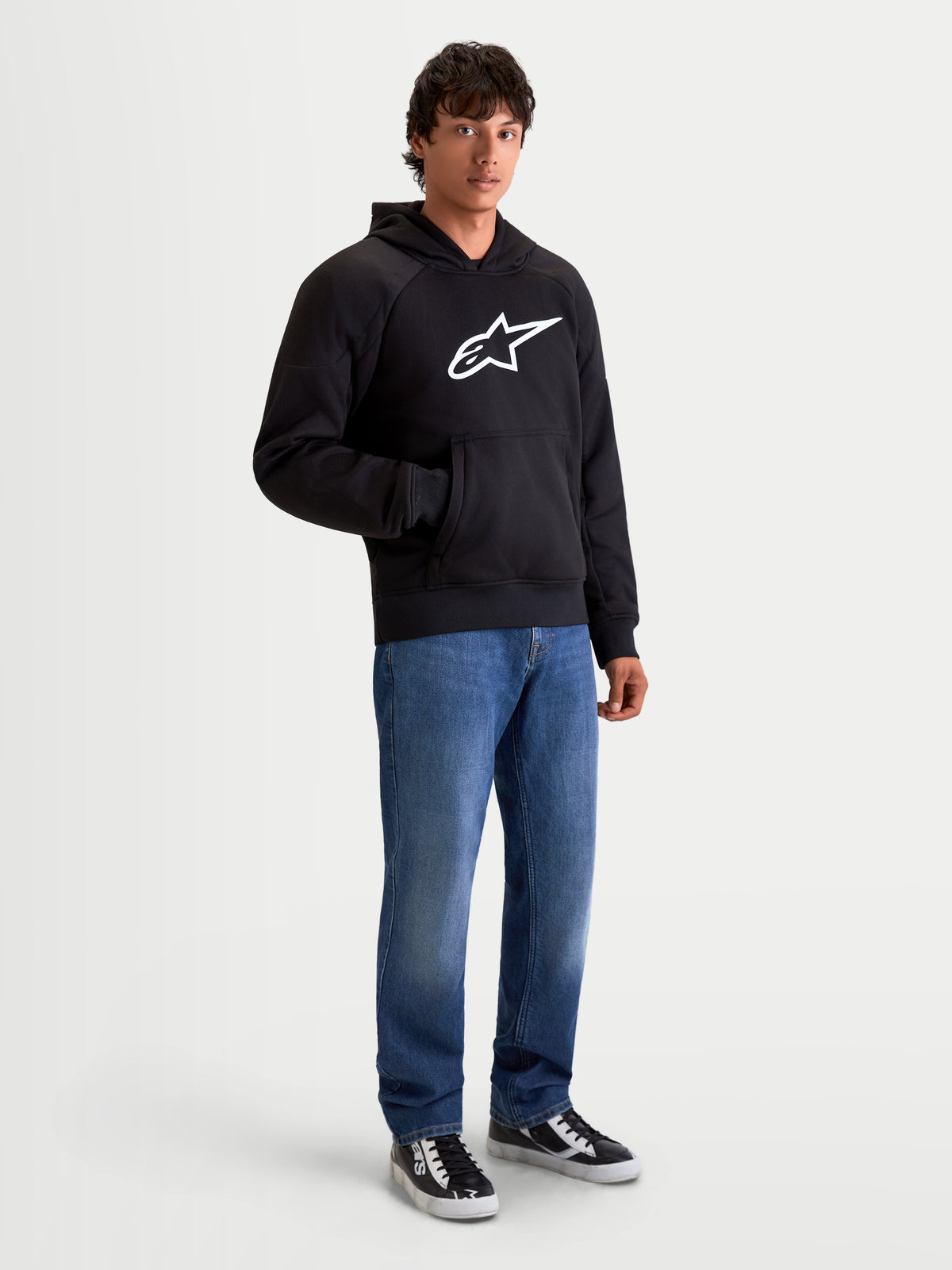 Alpinestars Chaqueta Con Capucha Ageless, sudadera de moto para hombre de estilo urbano en negro y blanco, vista frontal en modelo con vaqueros y logotipo en el pecho