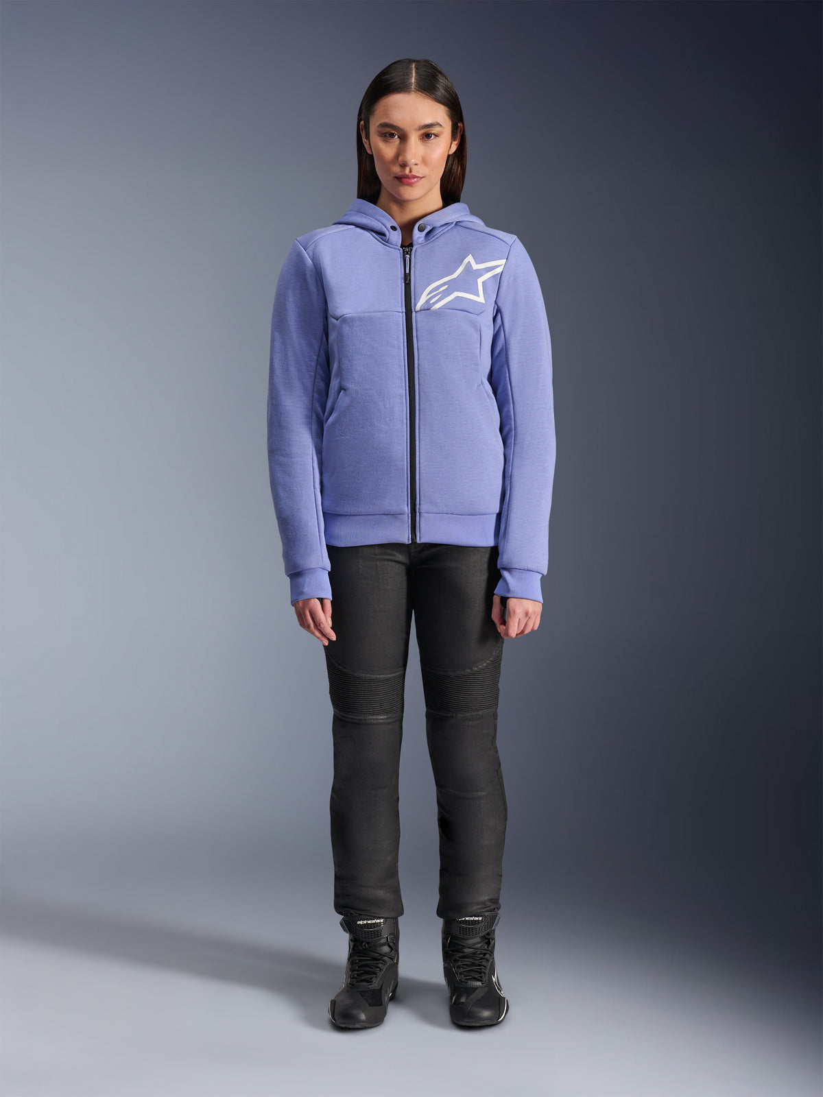Alpinestars Stella Chrome V2 Sport Hoodie para mujer, color violeta azulado con logotipo Astars blanco en el pecho, sudadera técnica de forro polar con cremallera completa y capucha, combinada con pantalones de moto negros y botas de conducción, equipamiento de conducción urbana casual para mujer
