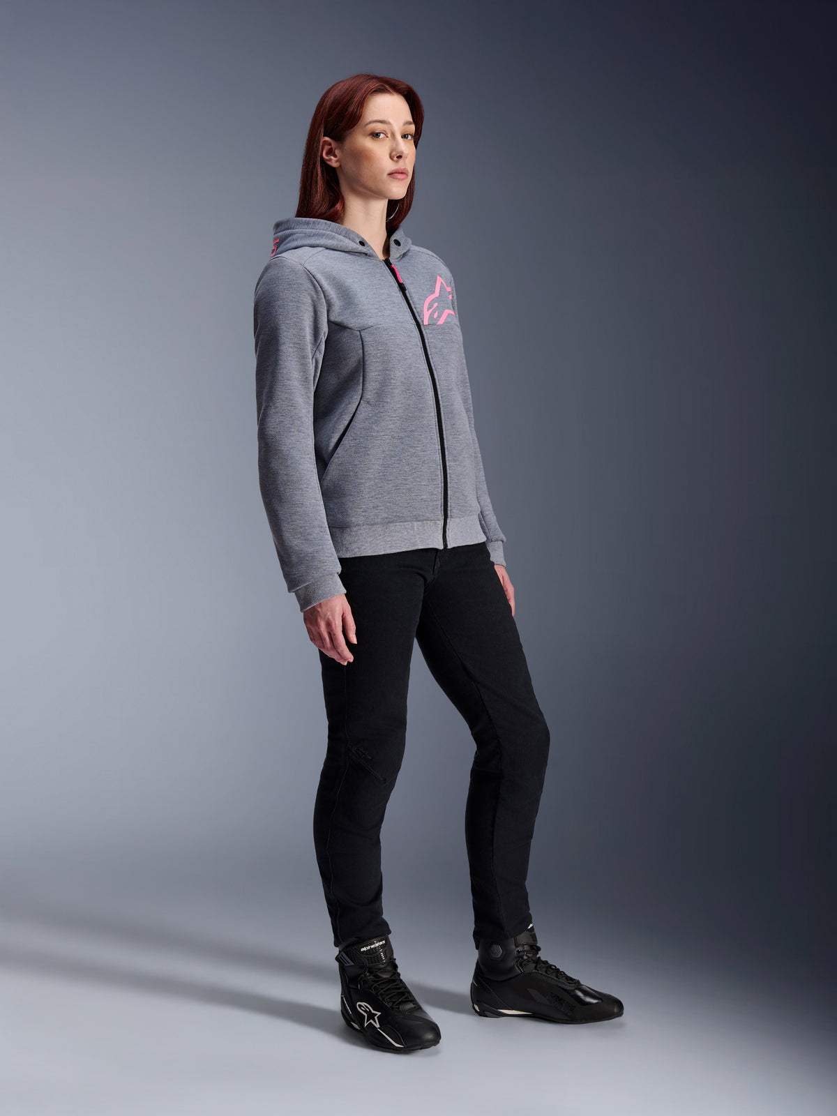 Alpinestars Stella Chrome V2 Sport Hoodie, sudadera de moto para mujer, gris jaspeado y rosa flúor, combinada con pantalones de conducción negros y botas negras, equipamiento de conducción urbana casual